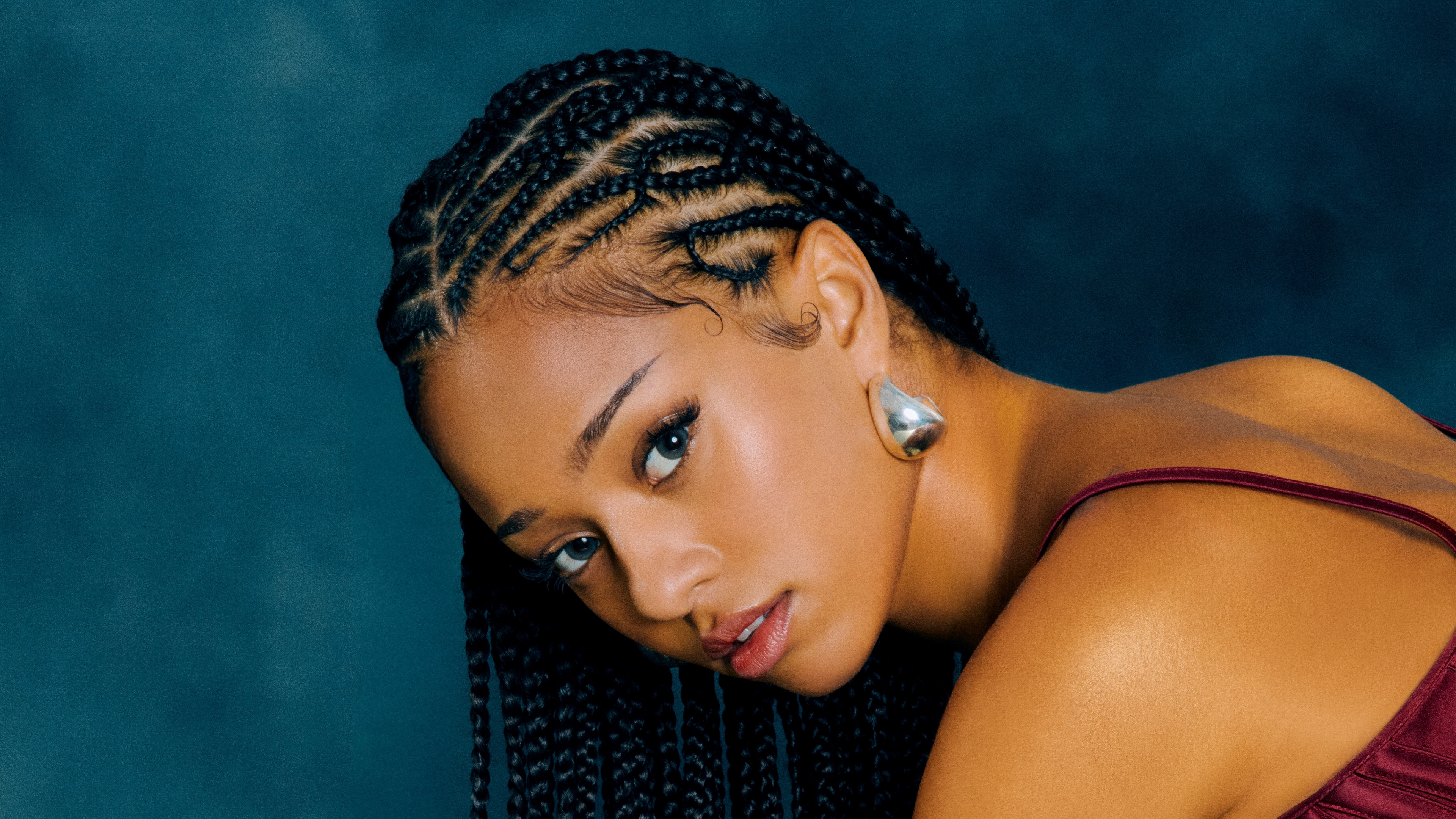 A close-up portrait of Manon from KATSEYE featuring beautiful burgundy braided hair.