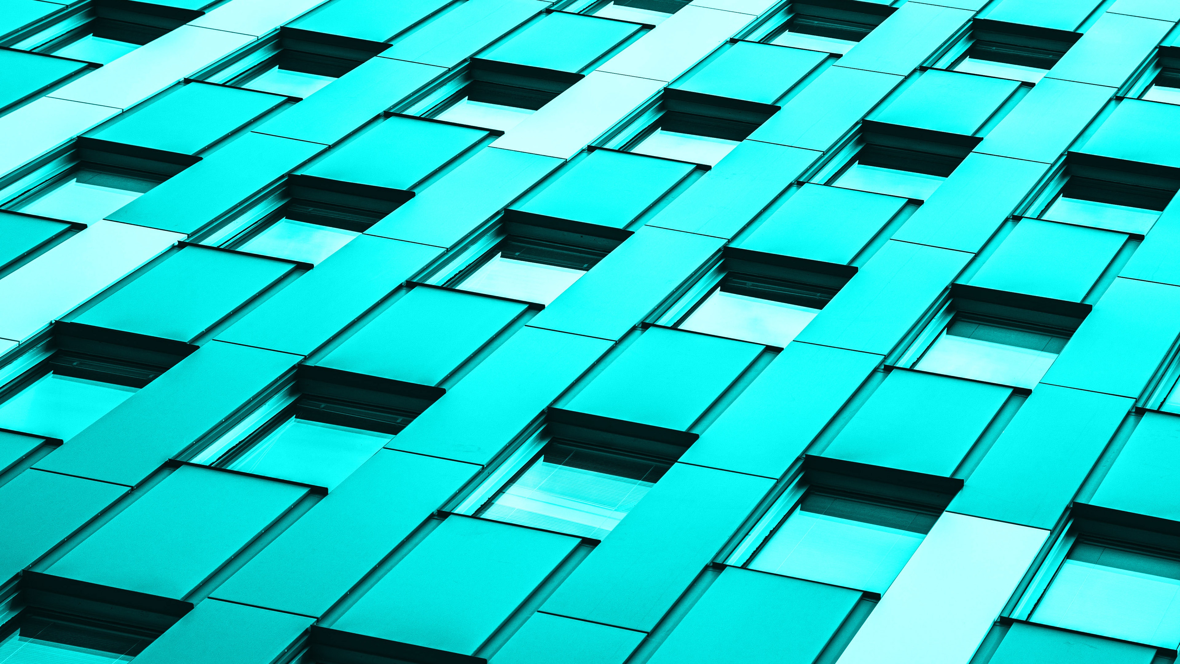 A modern glass office building with a vibrant teal and turquoise architectural design.