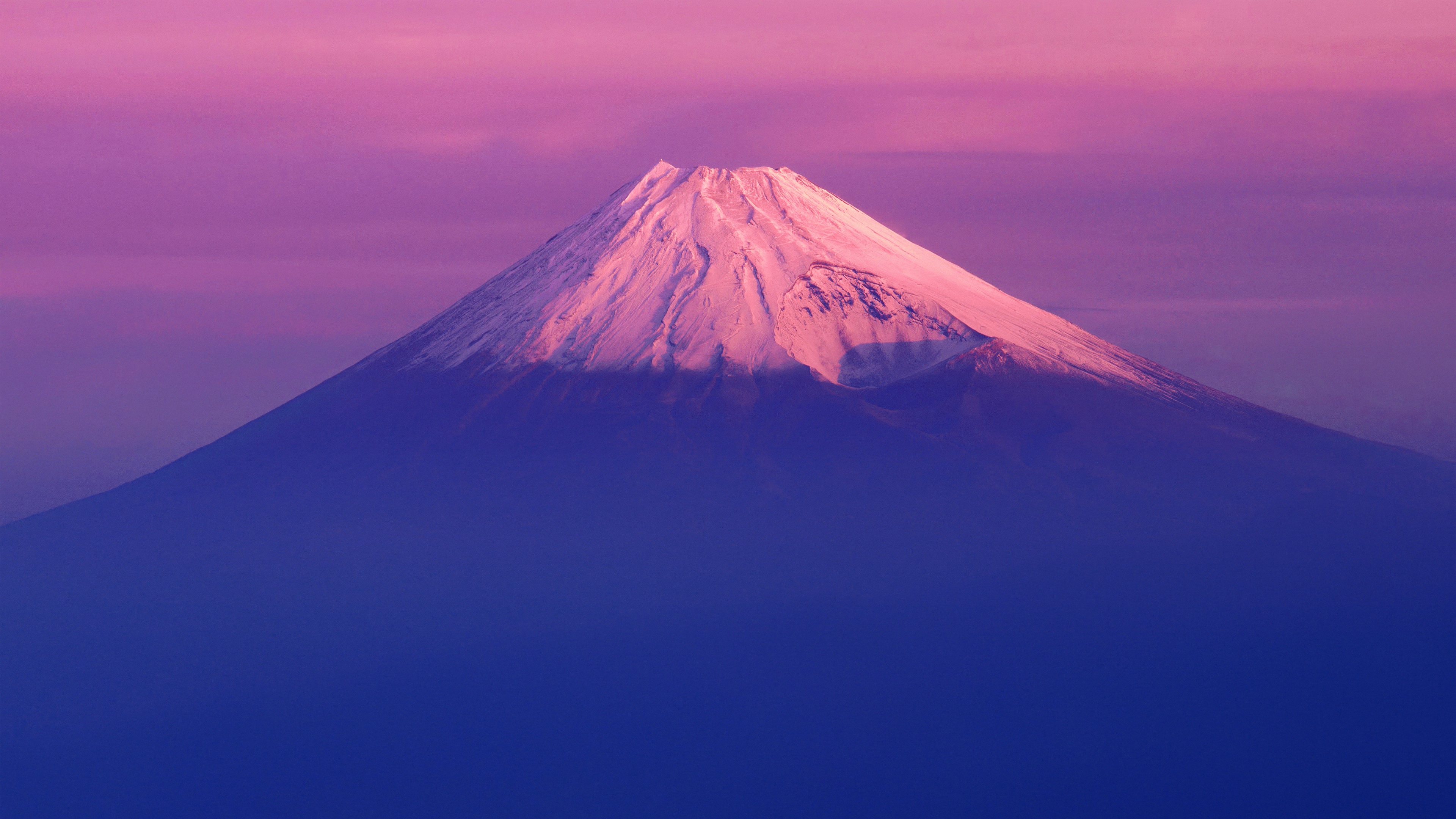 A stunning landscape of Mount Fuji at sunset with a soft pink sky, styled like a Mac OS X Lion wallpaper.