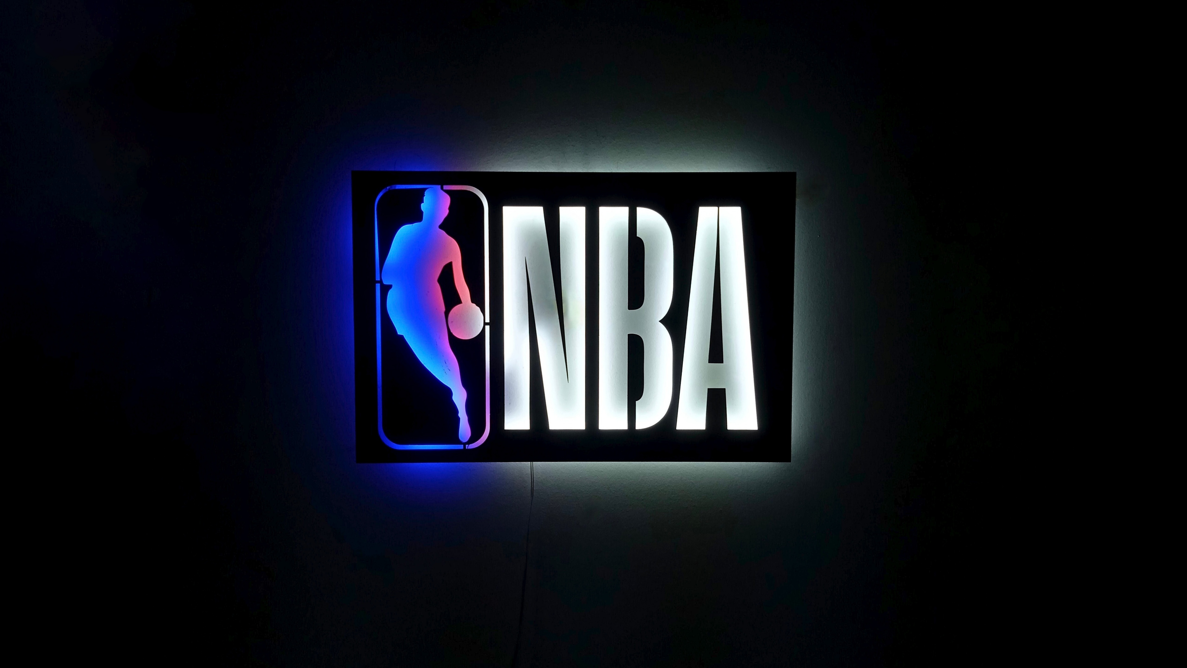 A glowing neon basketball logo with NBA branding on a dark background.