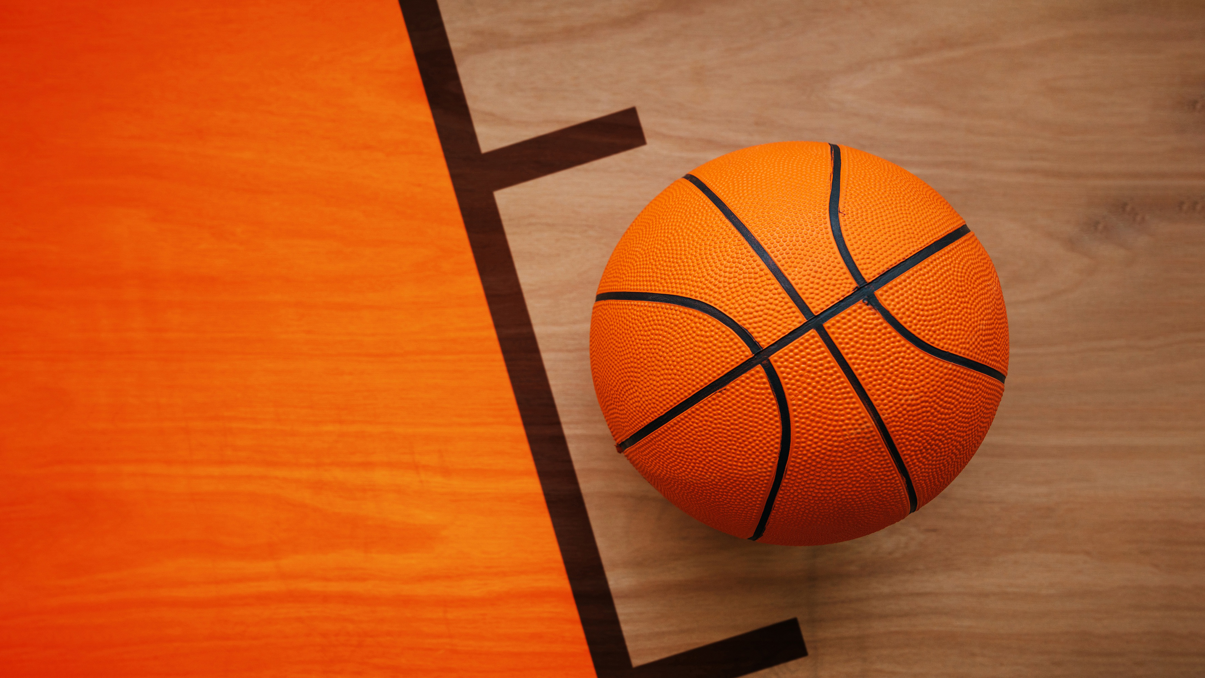 A high-angle view of a polished wooden basketball court showing reflective hardwood texture.