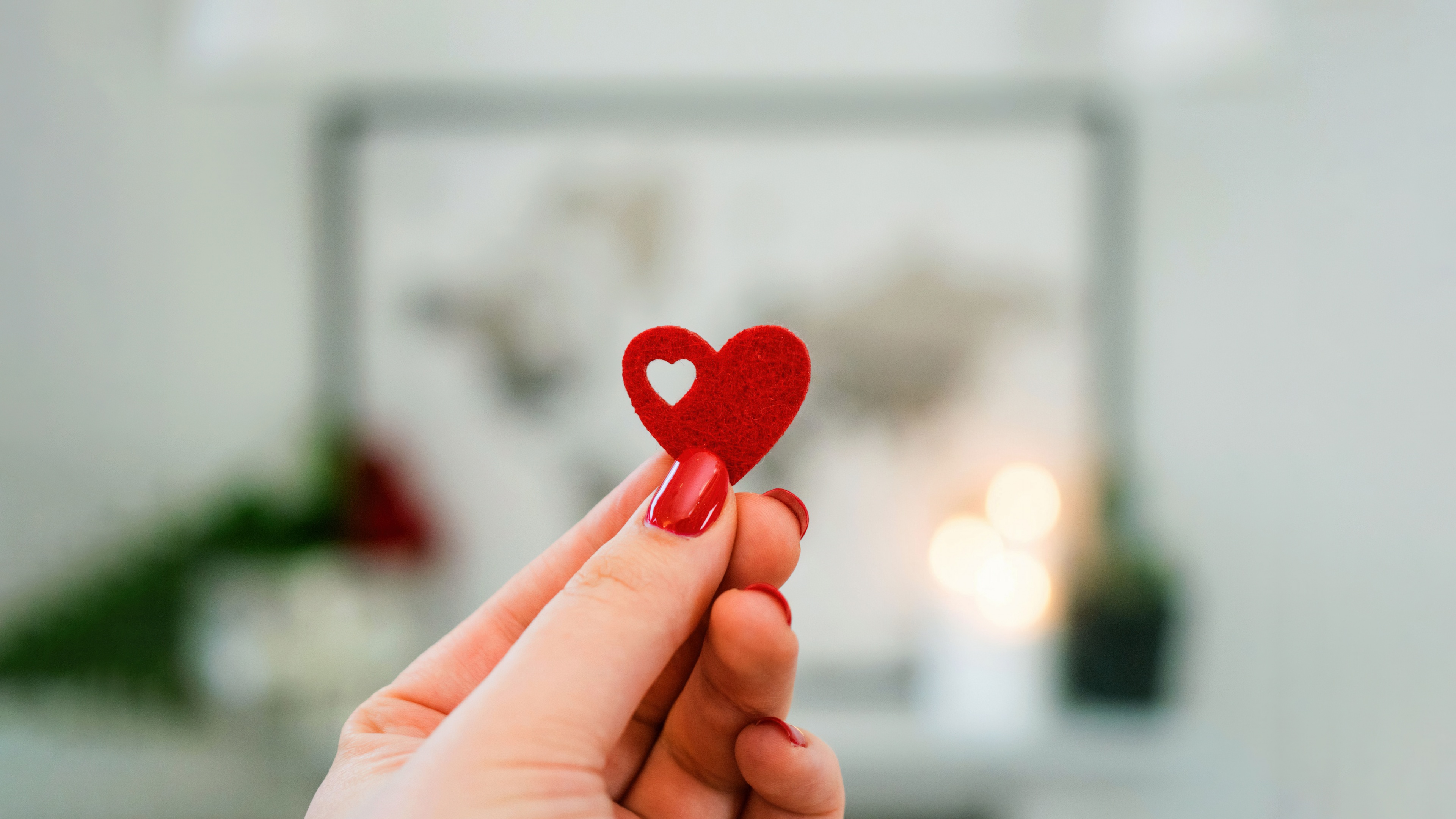A hand holding a bright red heart against a soft-focus bokeh background