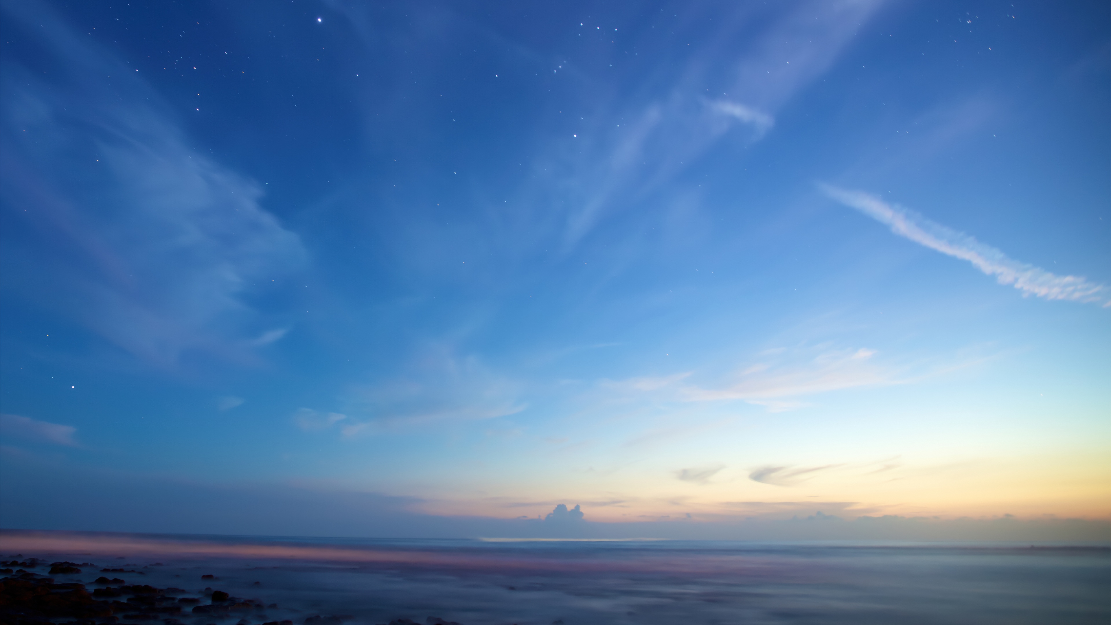 A wide-angle landscape of a bright sunrise over a mountain horizon with a clear blue sky and fluffy clouds.