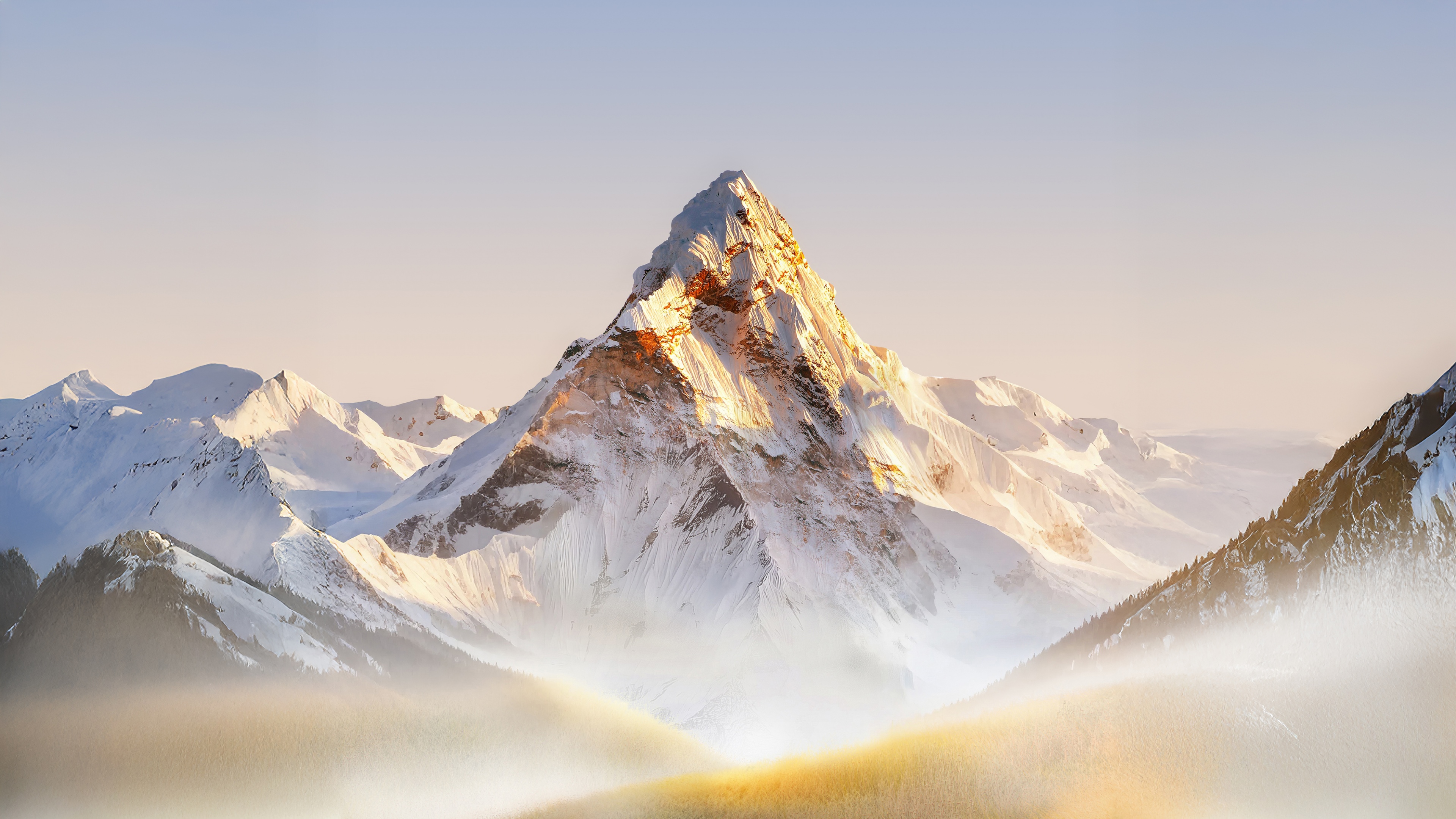 Snow-covered mountain range under bright sunlight with light fog and misty atmosphere.