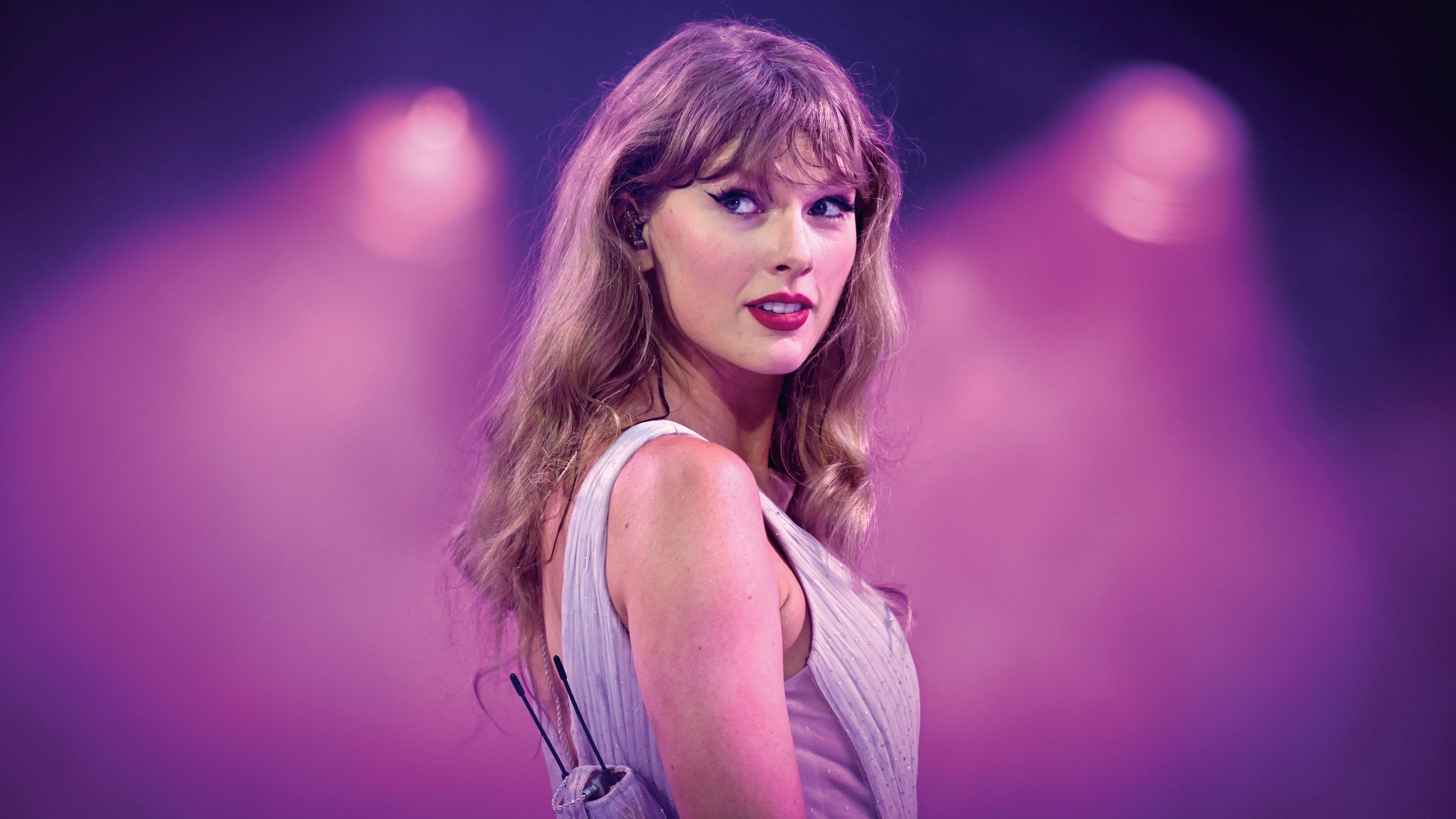 Taylor Swift performing on stage during a live concert featuring a vibrant pink aesthetic and stage lights.