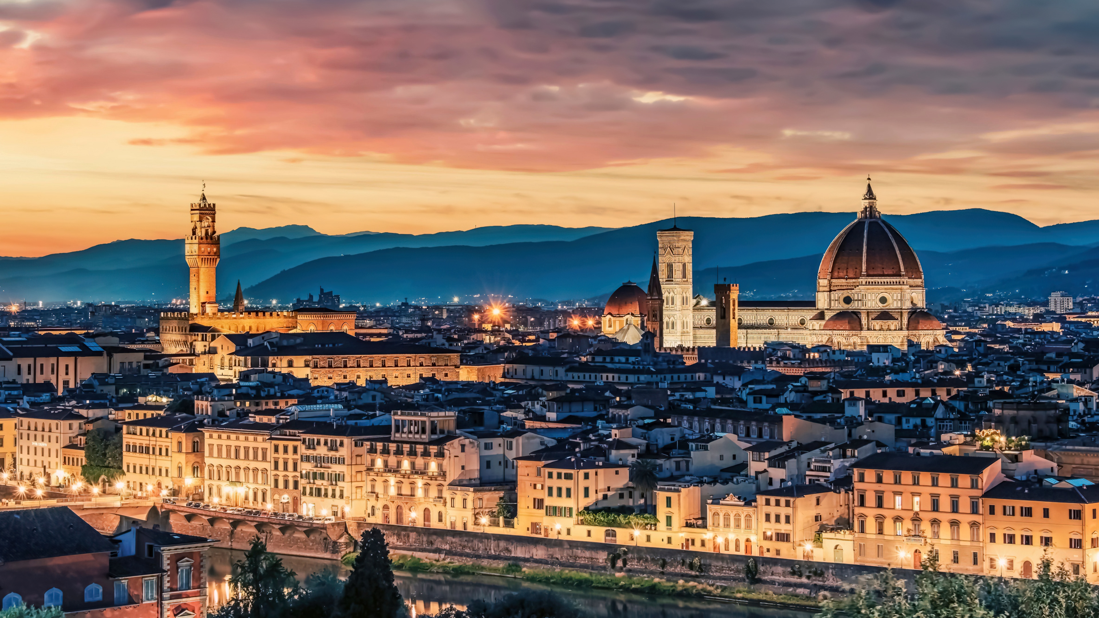 Sunset over an Italian cityscape featuring a historic church and glowing night lights.