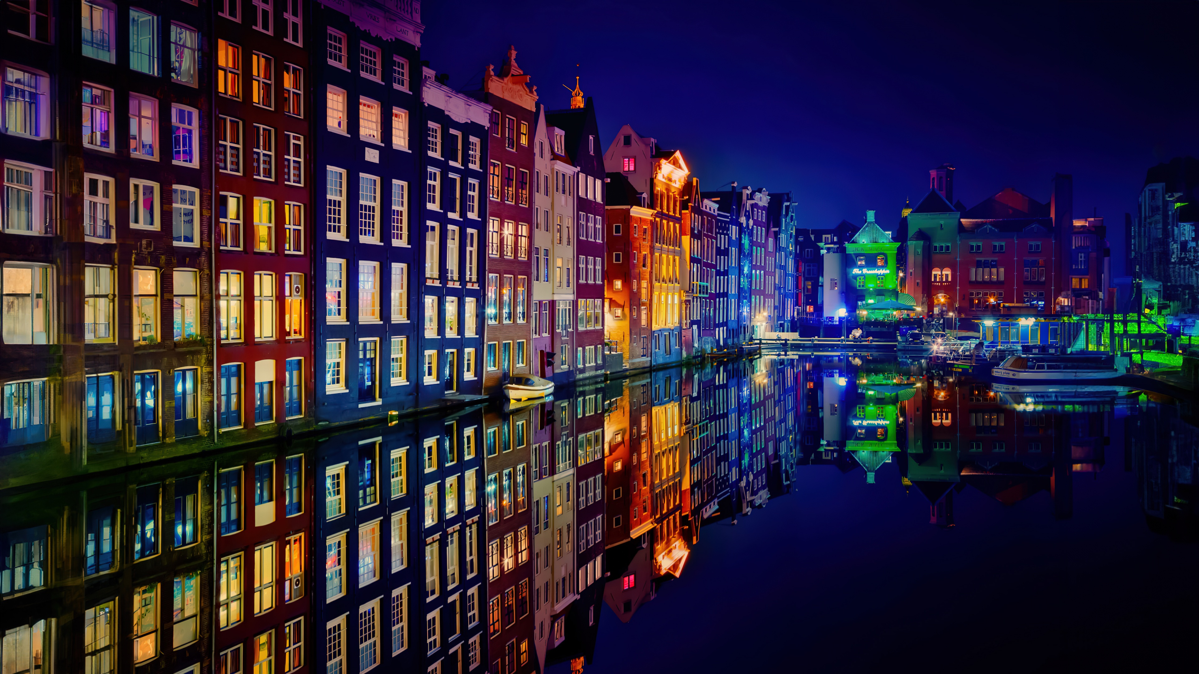 Colorful night view of Amsterdam buildings and canal reflections.