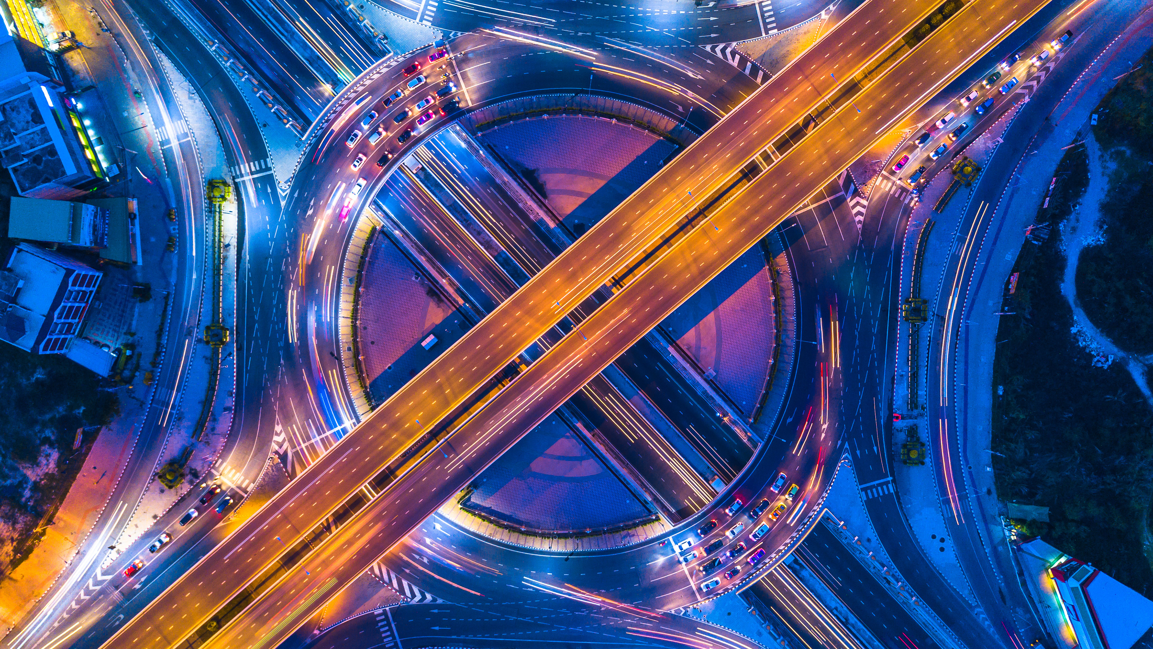 Aerial view of a Bangkok city intersection at night with long exposure light trails from moving traffic.