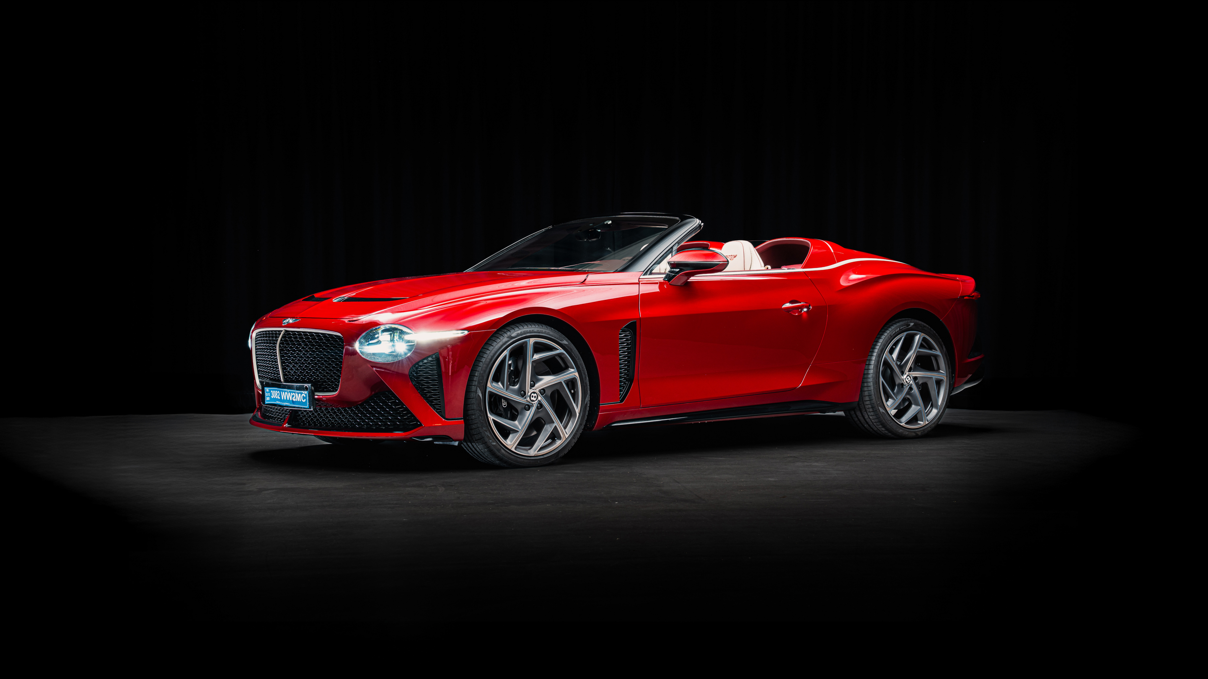 A luxury red Bentley Mulliner Bacalar convertible captured in high resolution against a dark, moody backdrop.
