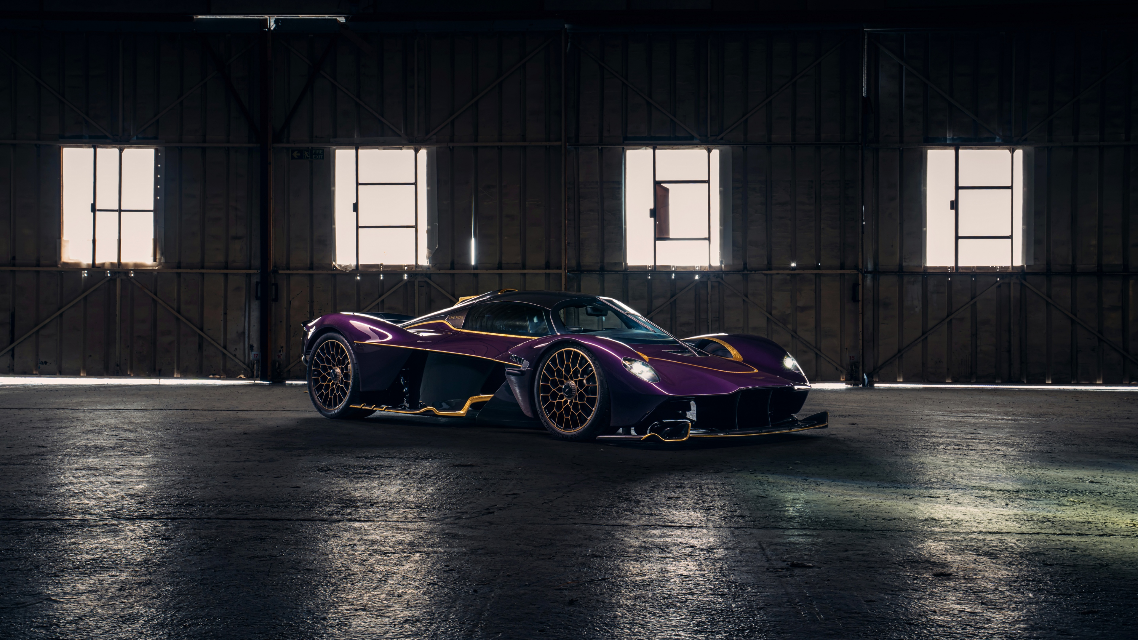 A purple Aston Martin Valkyrie hypercar parked inside a contemporary industrial hangar.