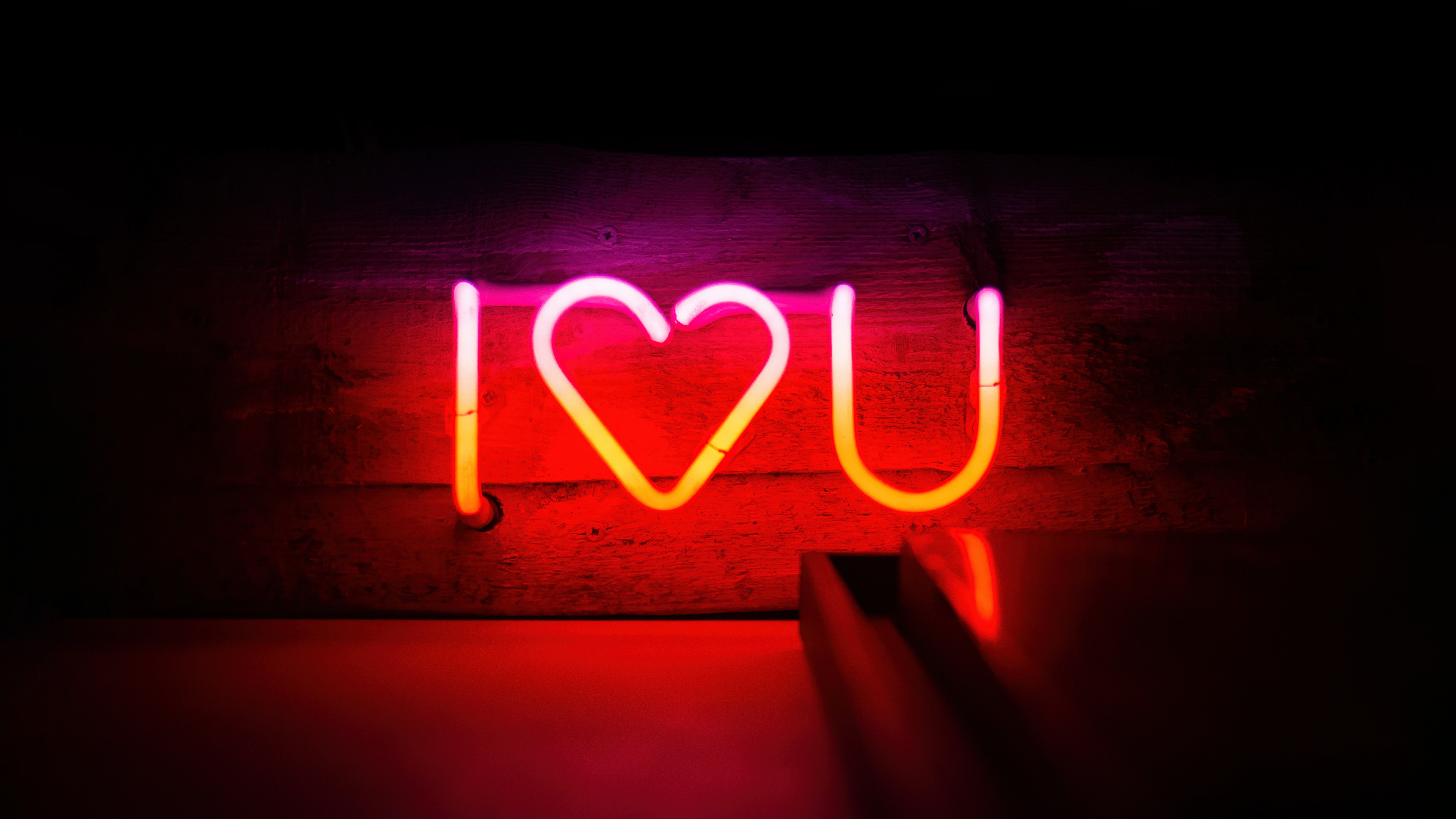 A bright, glowing neon sign that says 'I Love You' set against a pitch-black background
