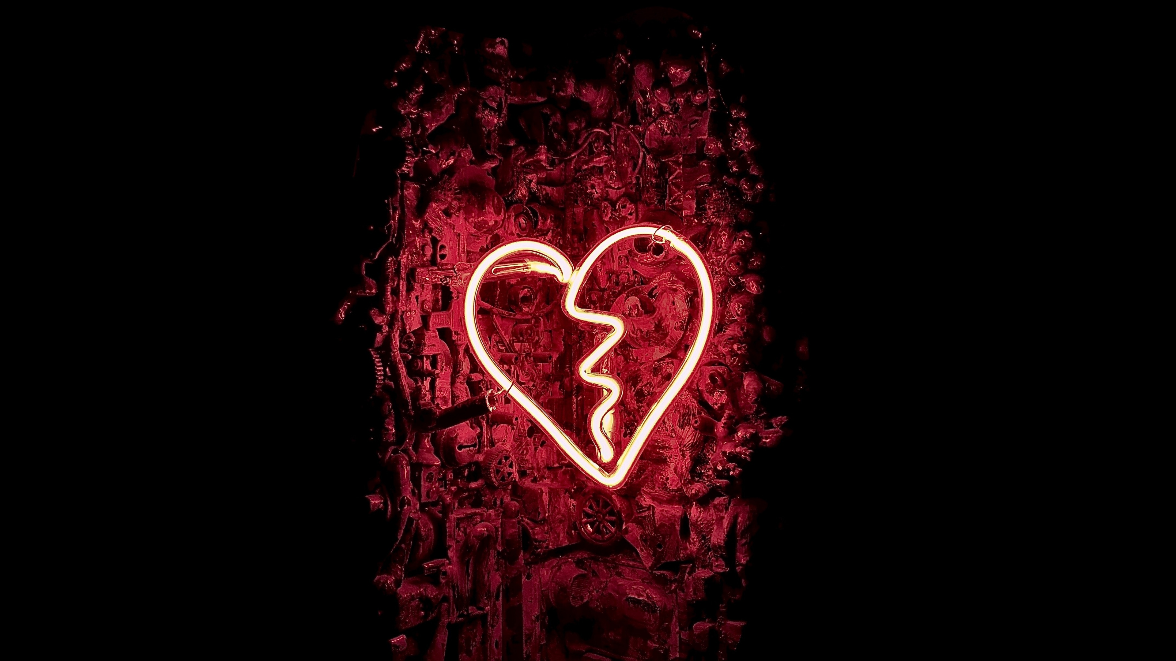 A glowing, shattered dark red neon heart sign against a dark background, symbolizing heartbreak.