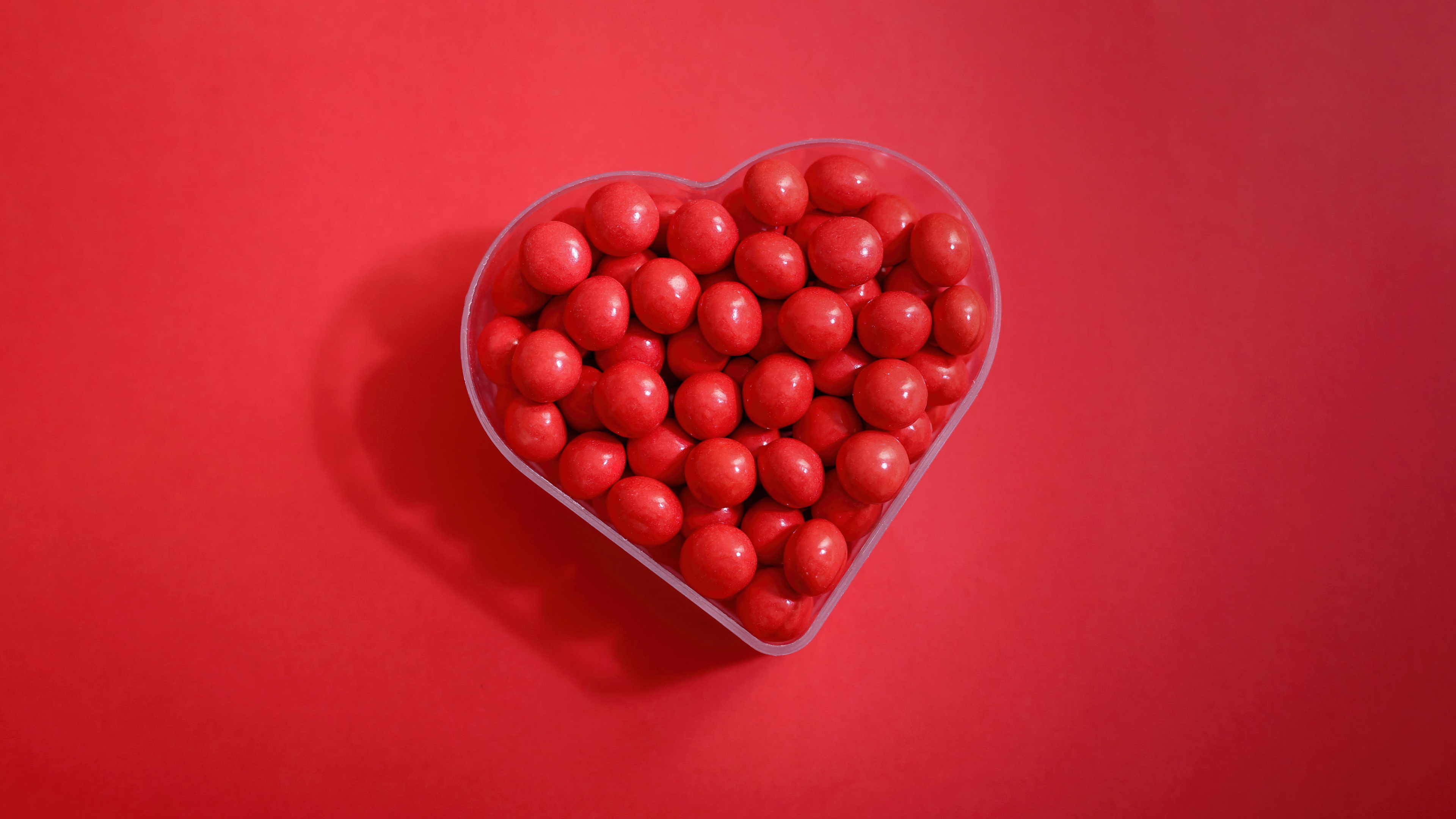A heart shape made of various colorful sugar candies set against a bright red background.