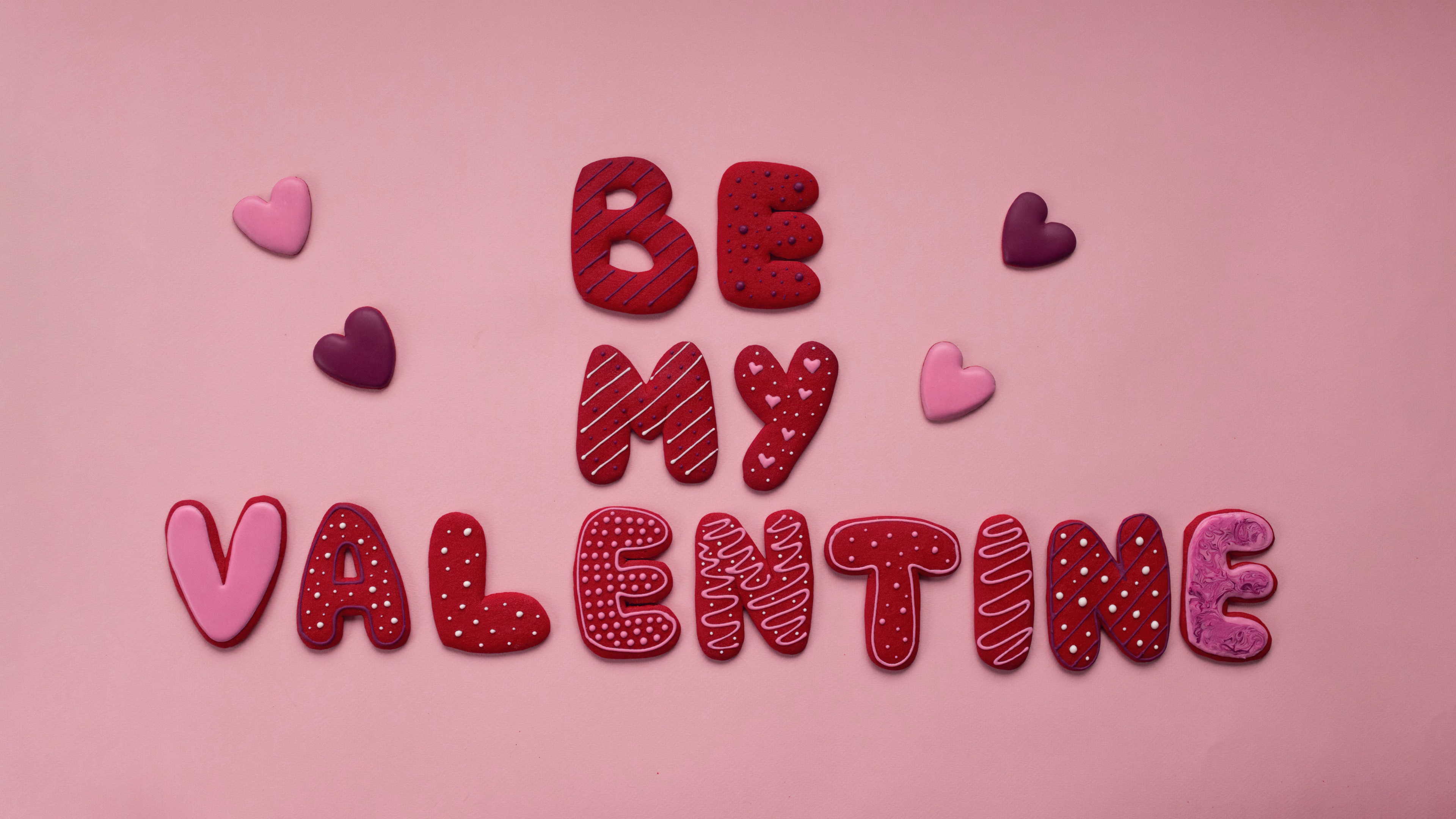 A soft pastel pink background decorated with various pink love hearts and the text 'Be My Valentine' in a romantic font.