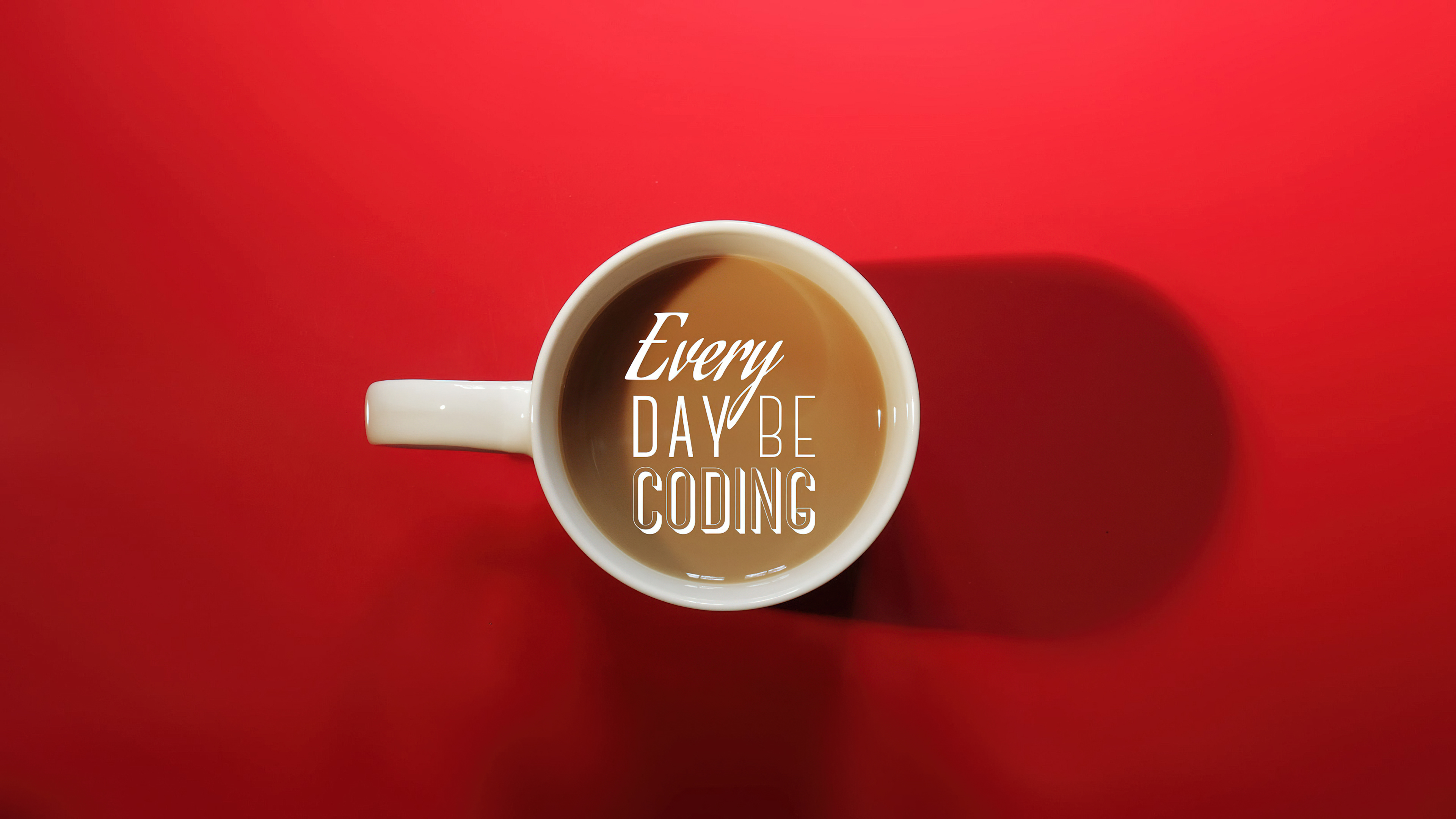 A programmer working on code next to a cup of coffee against a bright red background.