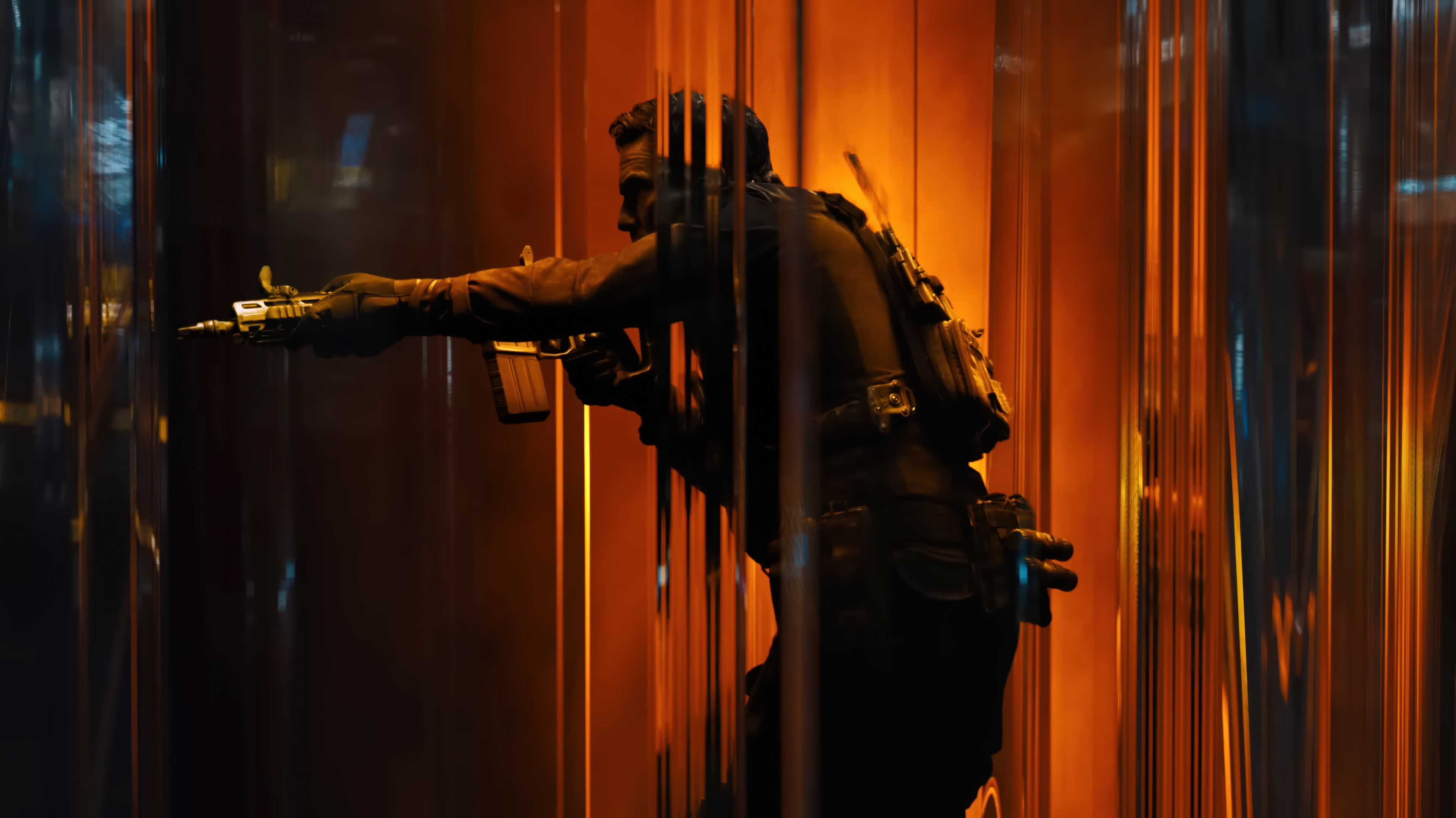 Silhouette of a tactical soldier in full combat gear holding a rifle against bright orange lighting.