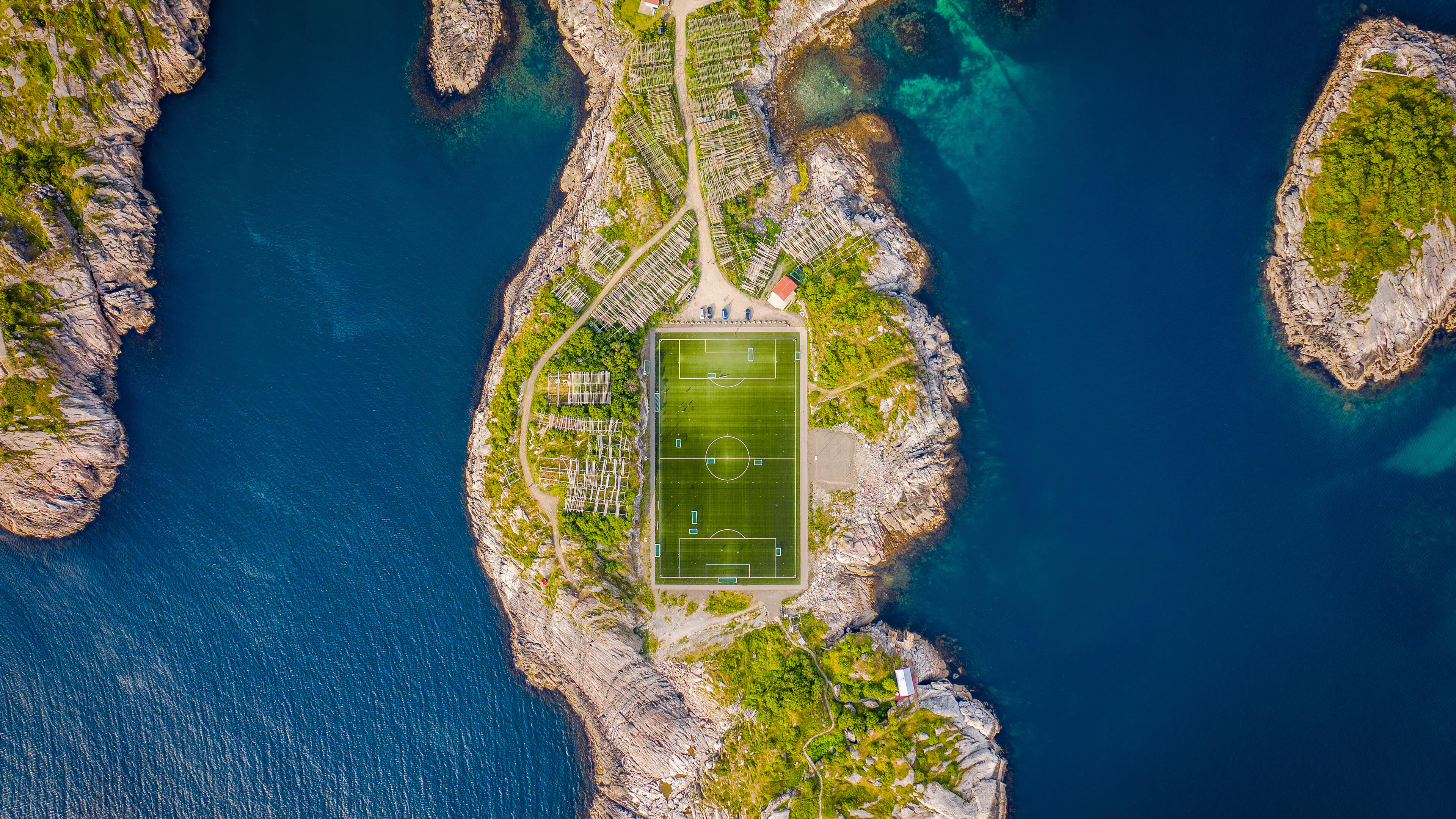 A high-angle aerial shot of a green soccer pitch situated in the beautiful Norwegian countryside.