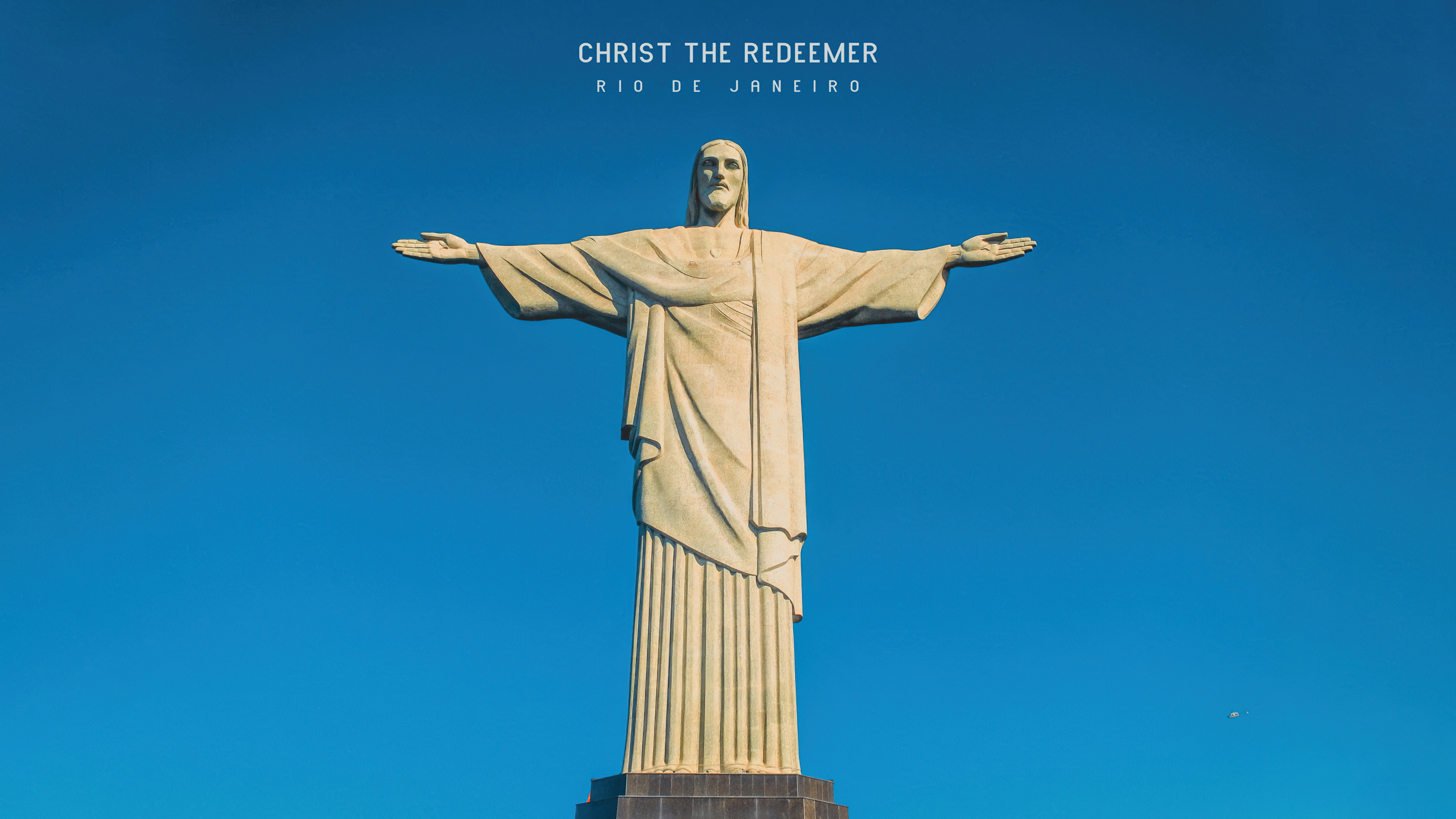 The Christ the Redeemer statue in Rio de Janeiro, Brazil, under a sunny blue sky.