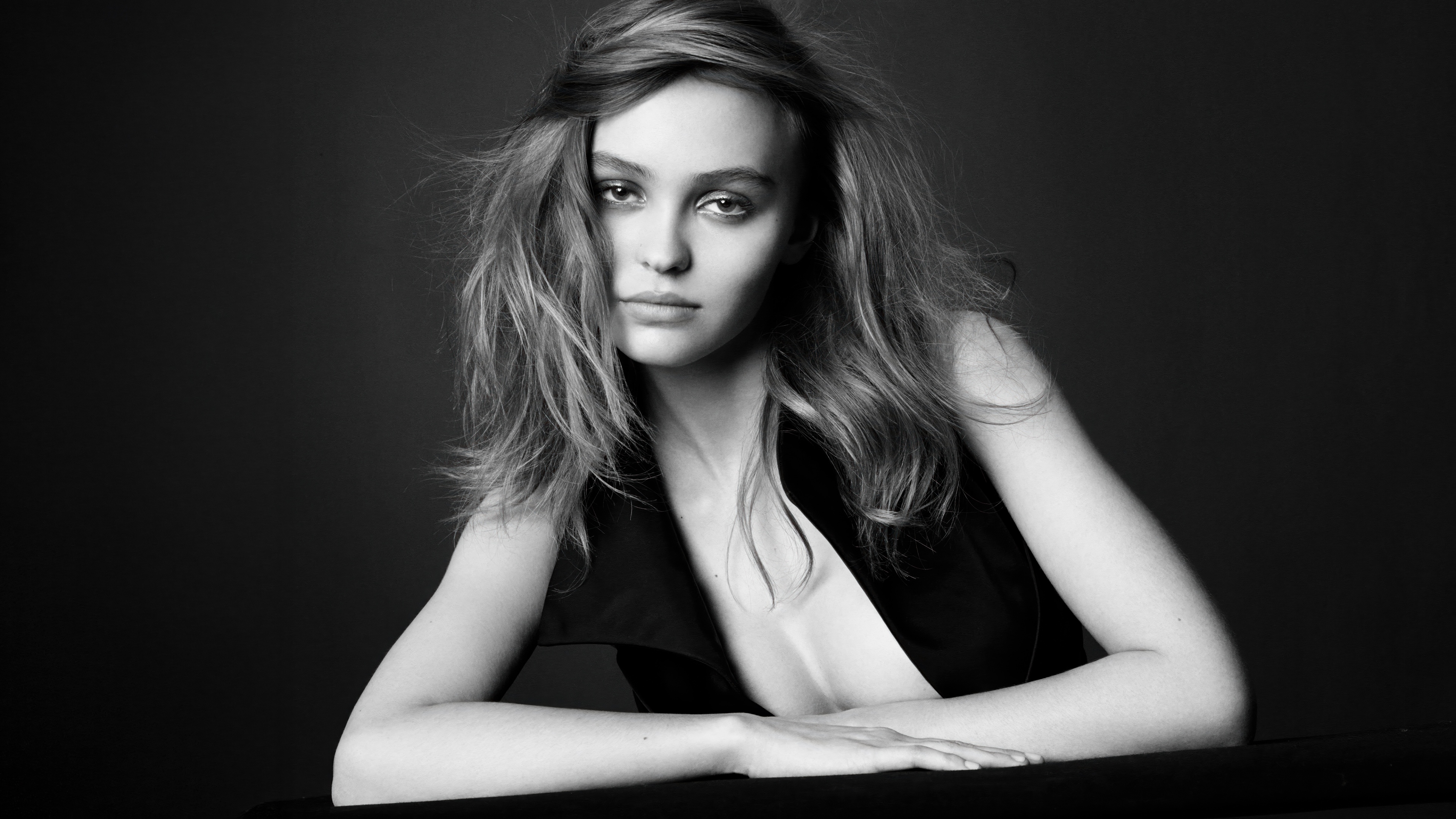 A dramatic black and white close-up portrait of Lily Rose Depp against a dark, minimalist background.