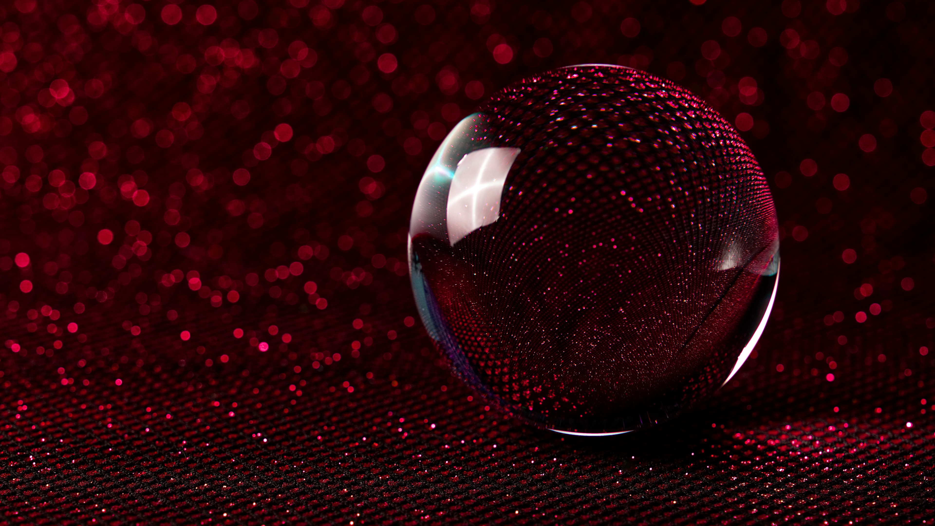 A macro close-up of a crystal ball with a dark red color palette and a soft, shimmering bokeh background.