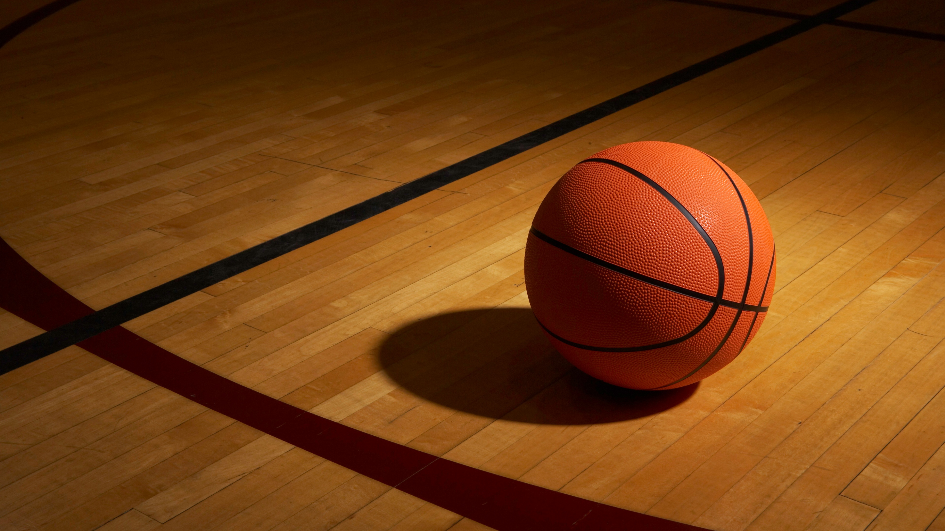 A close-up view of a basketball resting on the surface of a polished basketball court under dramatic lighting.