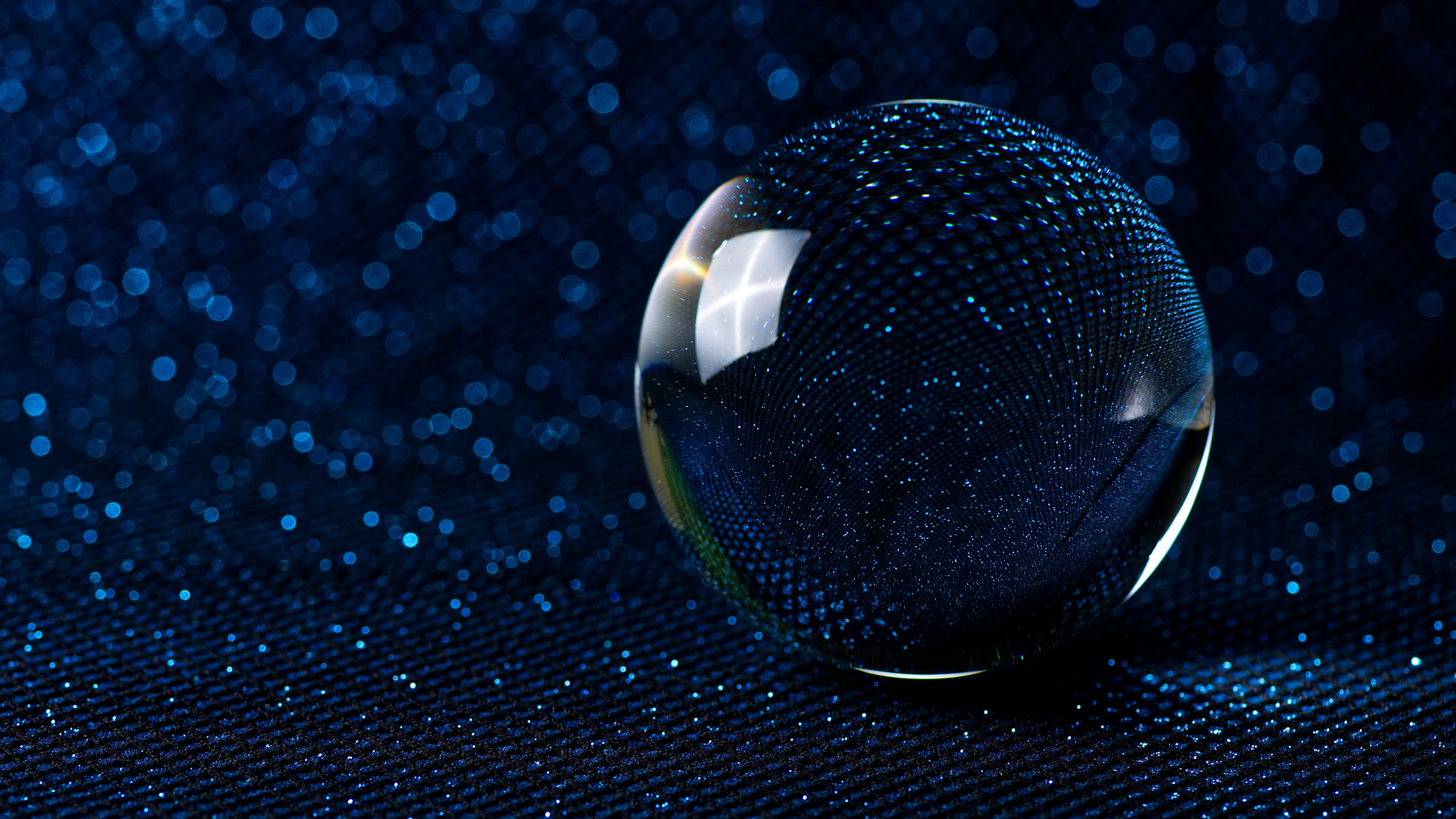 Macro photography of a dark blue crystal ball with shimmering bokeh lights in the background.