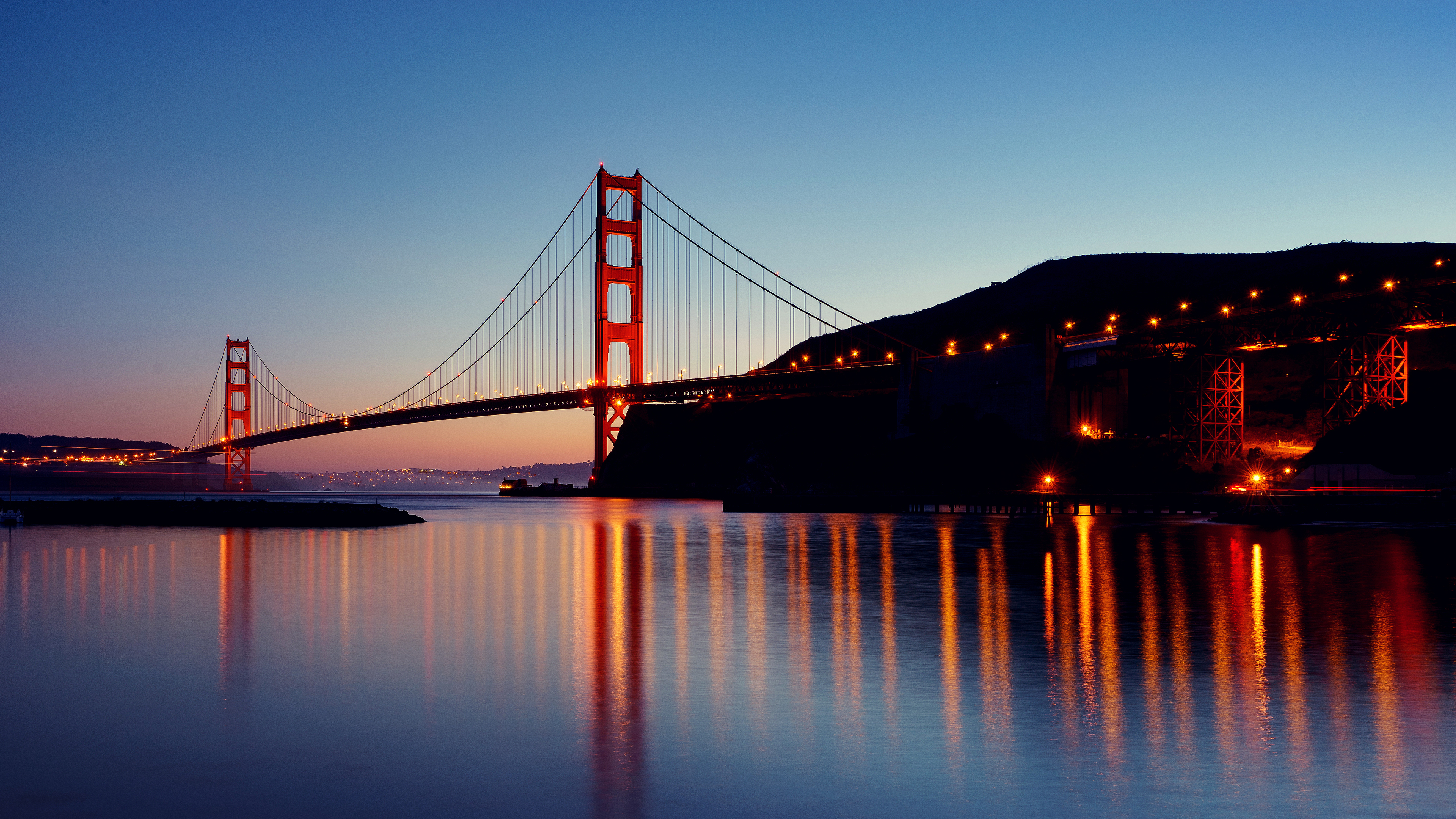 A scenic view of the Golden Gate Bridge in San Francisco at sunset with colorful reflections on the water.