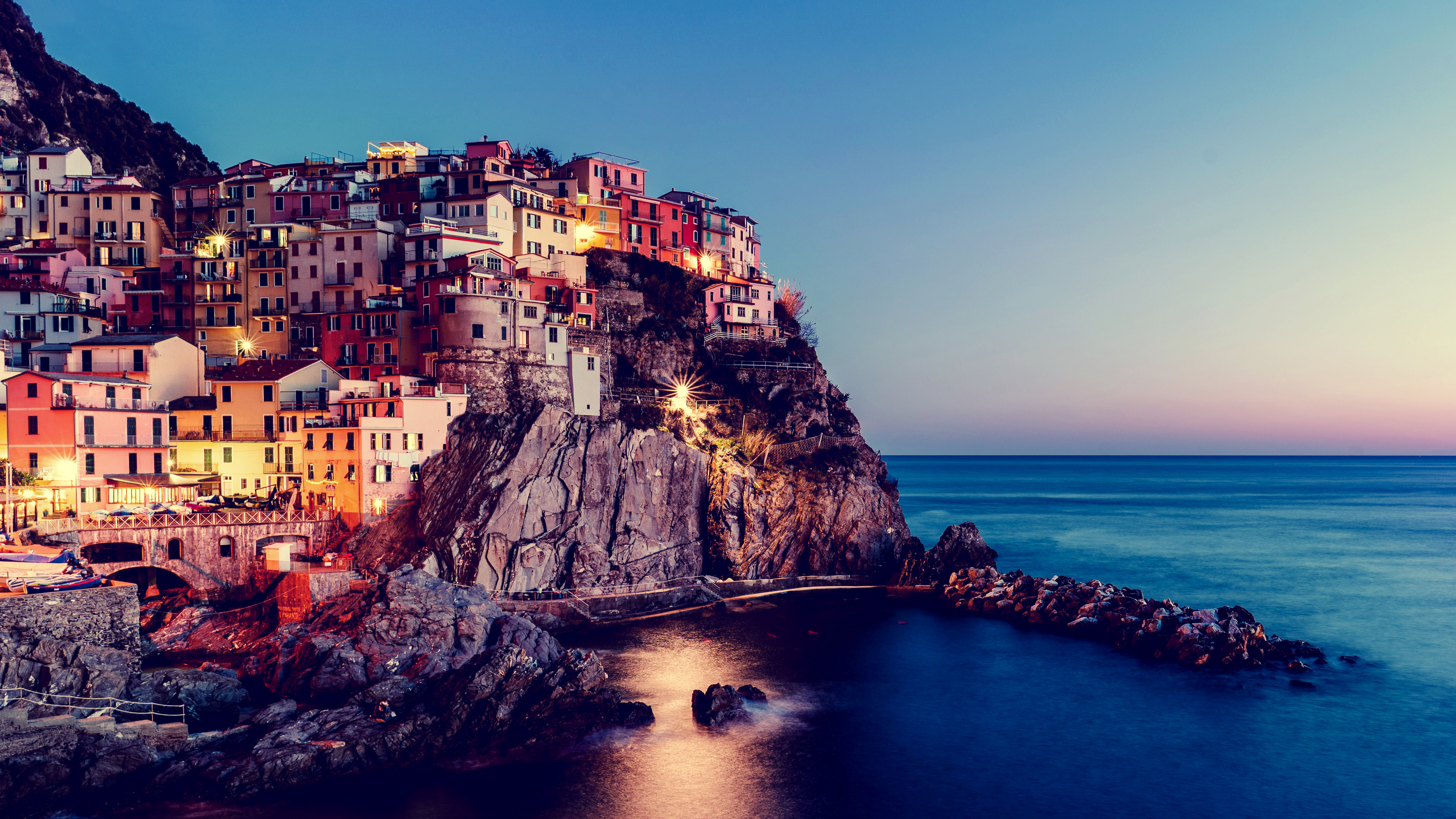 A scenic sunset view of the colorful coastal buildings of Manarola, Cinque Terre, Italy, under a twilight sky.