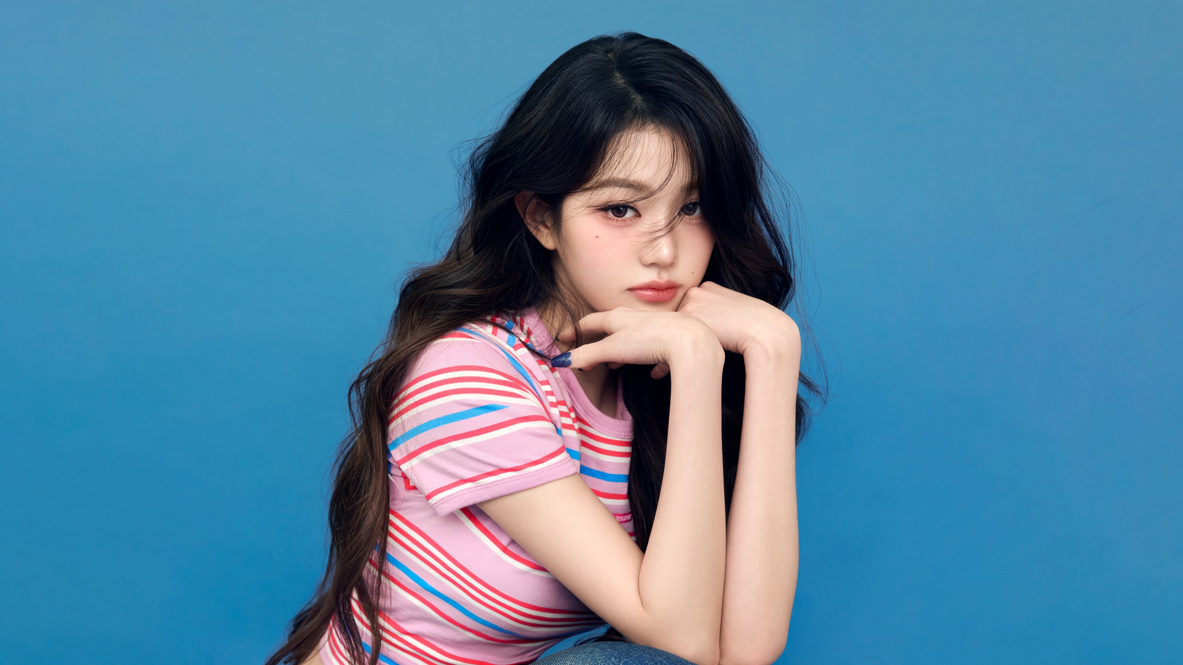 A high-resolution close-up of K-pop star Jang Wonyoung with a vivid blue background