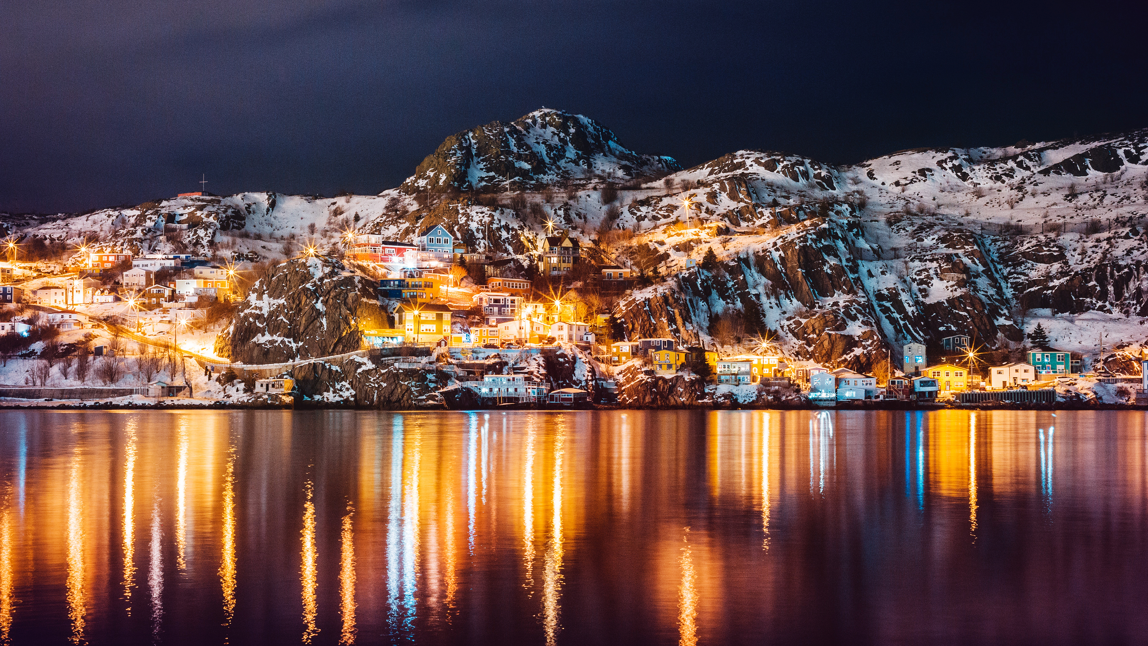 A nighttime view of a Canadian island with warm lights reflecting on the still surface of a dark lake.