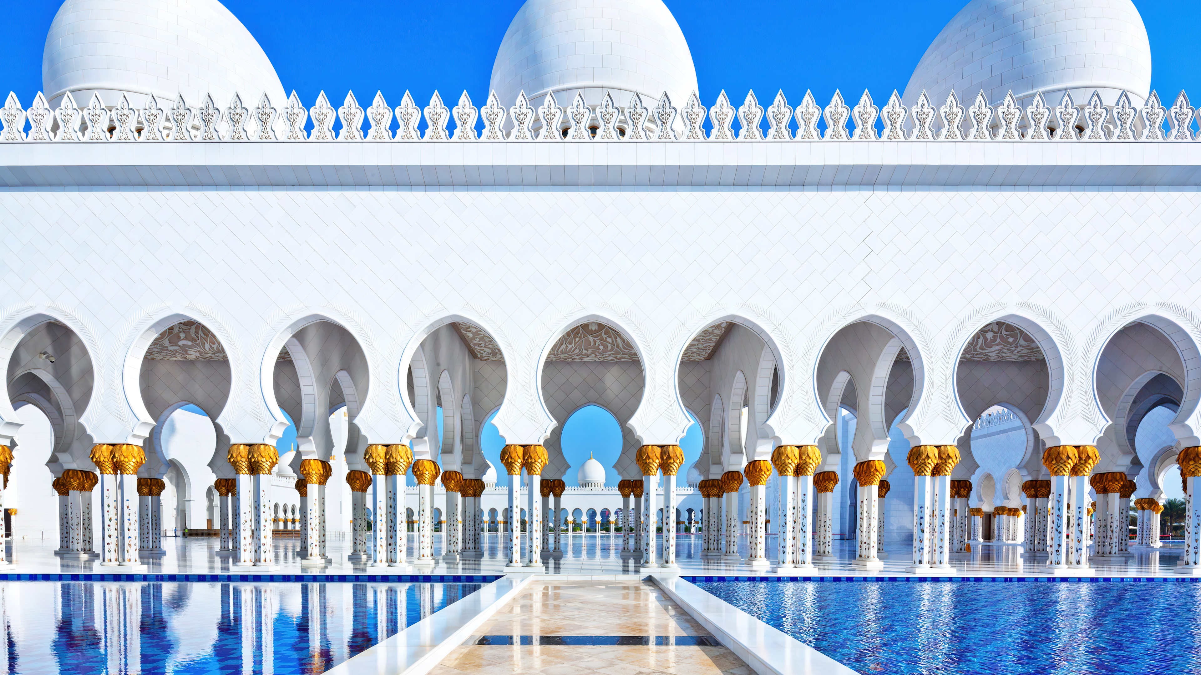 The magnificent white marble domes and minarets of the Sheikh Zayed Grand Mosque in Abu Dhabi, UAE, under a clear sky.