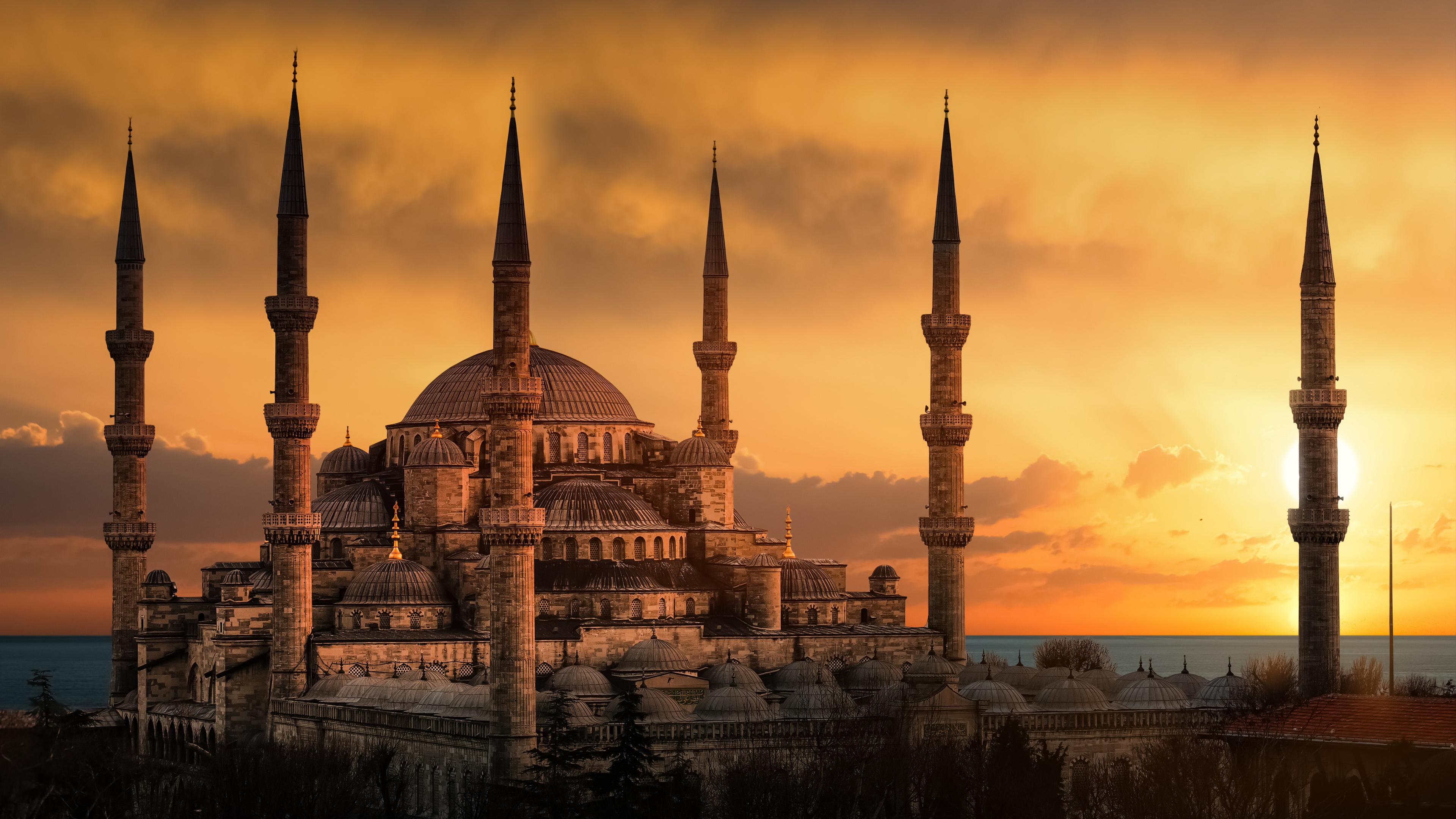 The Sultan Ahmed Mosque in Istanbul, Turkey, under a vibrant sunset sky with golden lighting on its ancient domes and minarets.