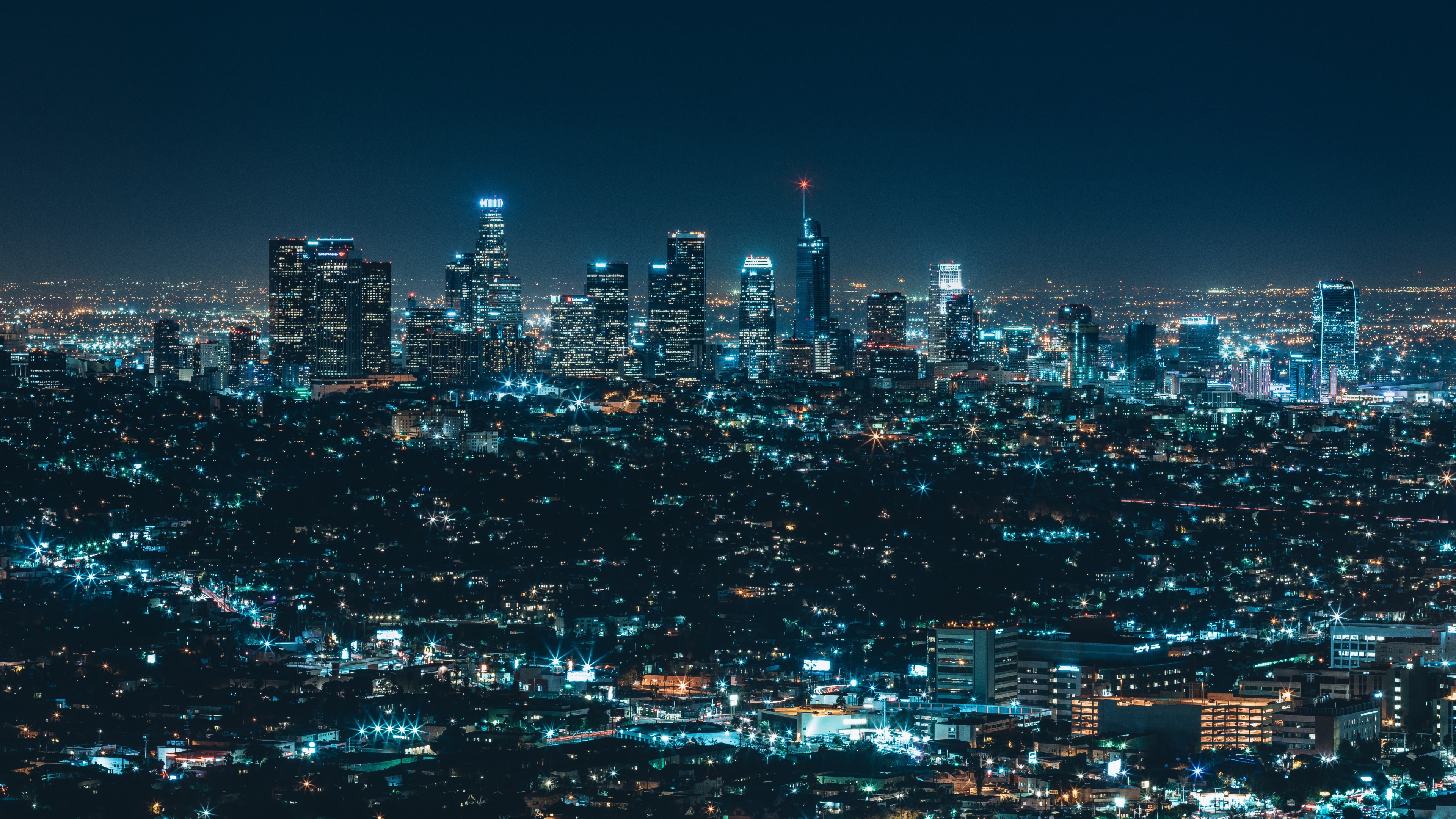 A luminous night view of the Los Angeles skyline with brightly lit skyscrapers and urban city lights.