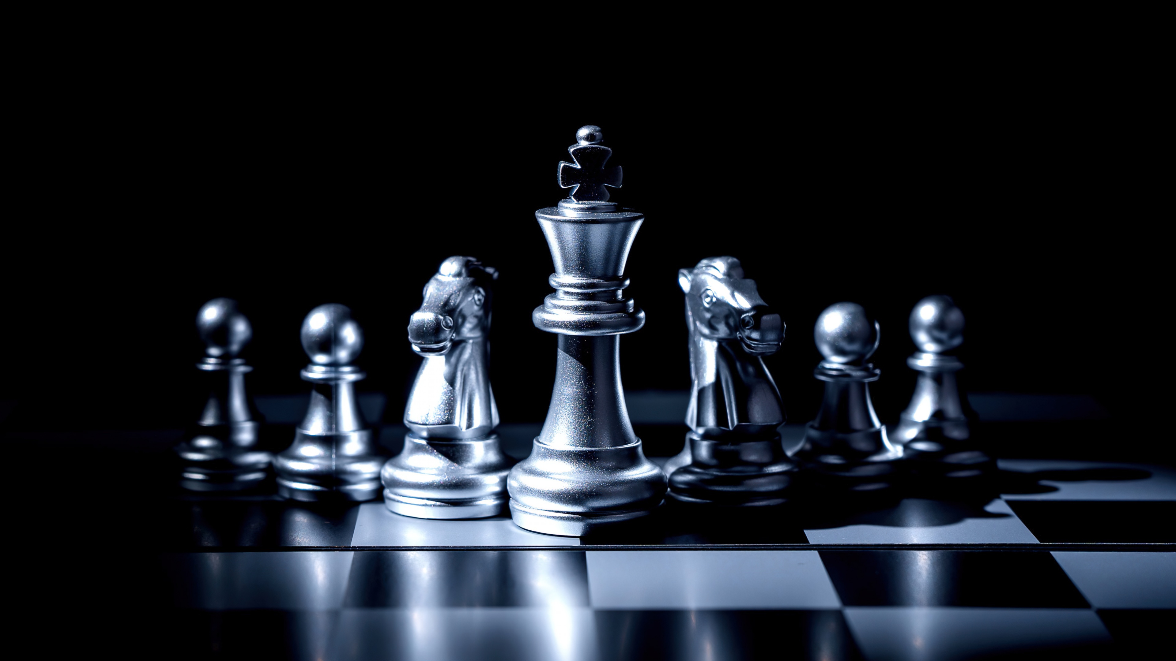 A high-contrast monochrome close-up of various chess pieces, including the King, Knight, and Rook, positioned on a chessboard.