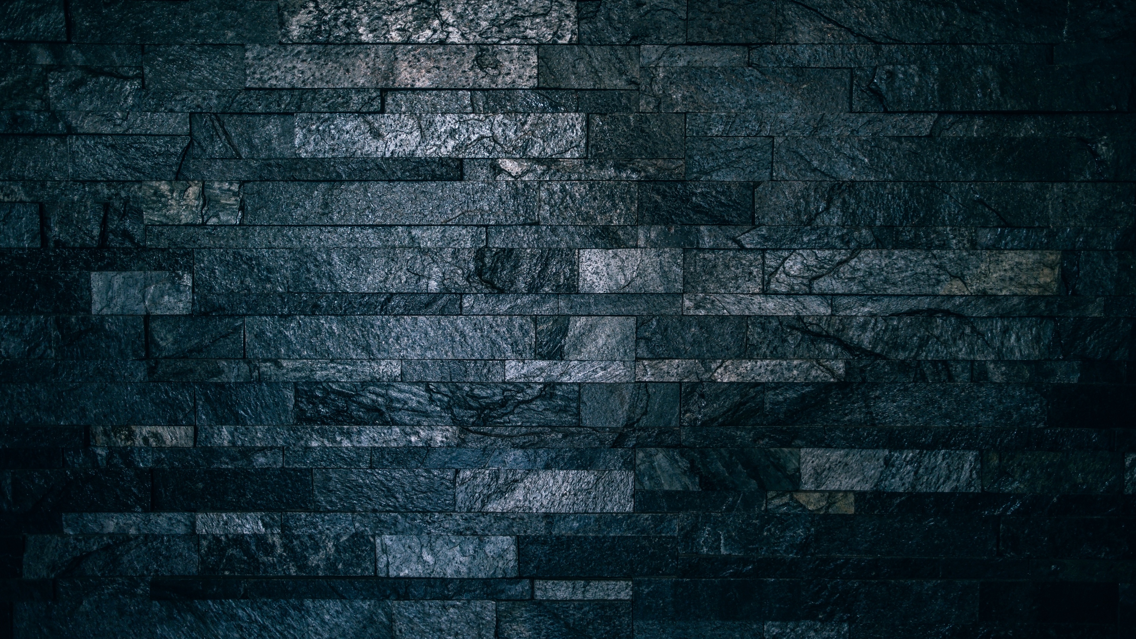 Close-up of a dark, textured brick wall in a low-light setting with deep shadows.