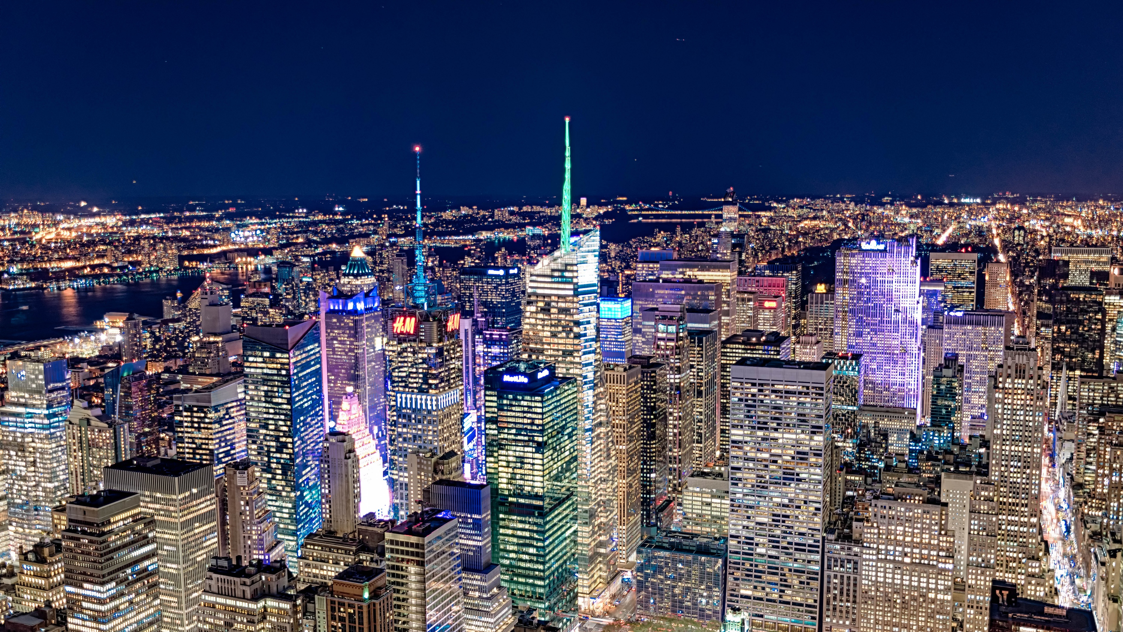 A panoramic night view of the New York City skyline featuring brightly lit skyscrapers and urban city lights.