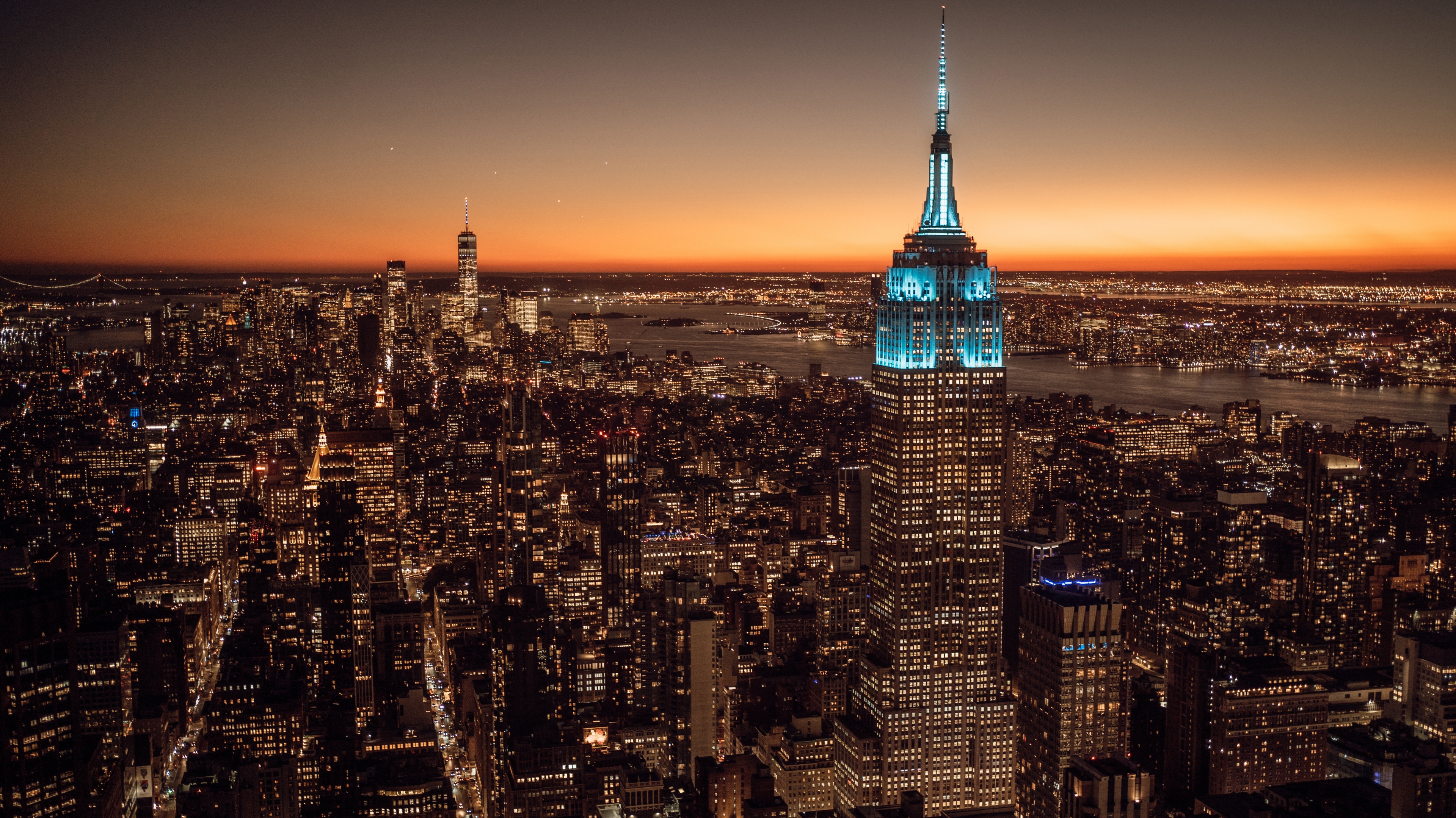 A stunning high-resolution cityscape of New York City featuring the Empire State Building under a colorful sunset with glowing city lights.