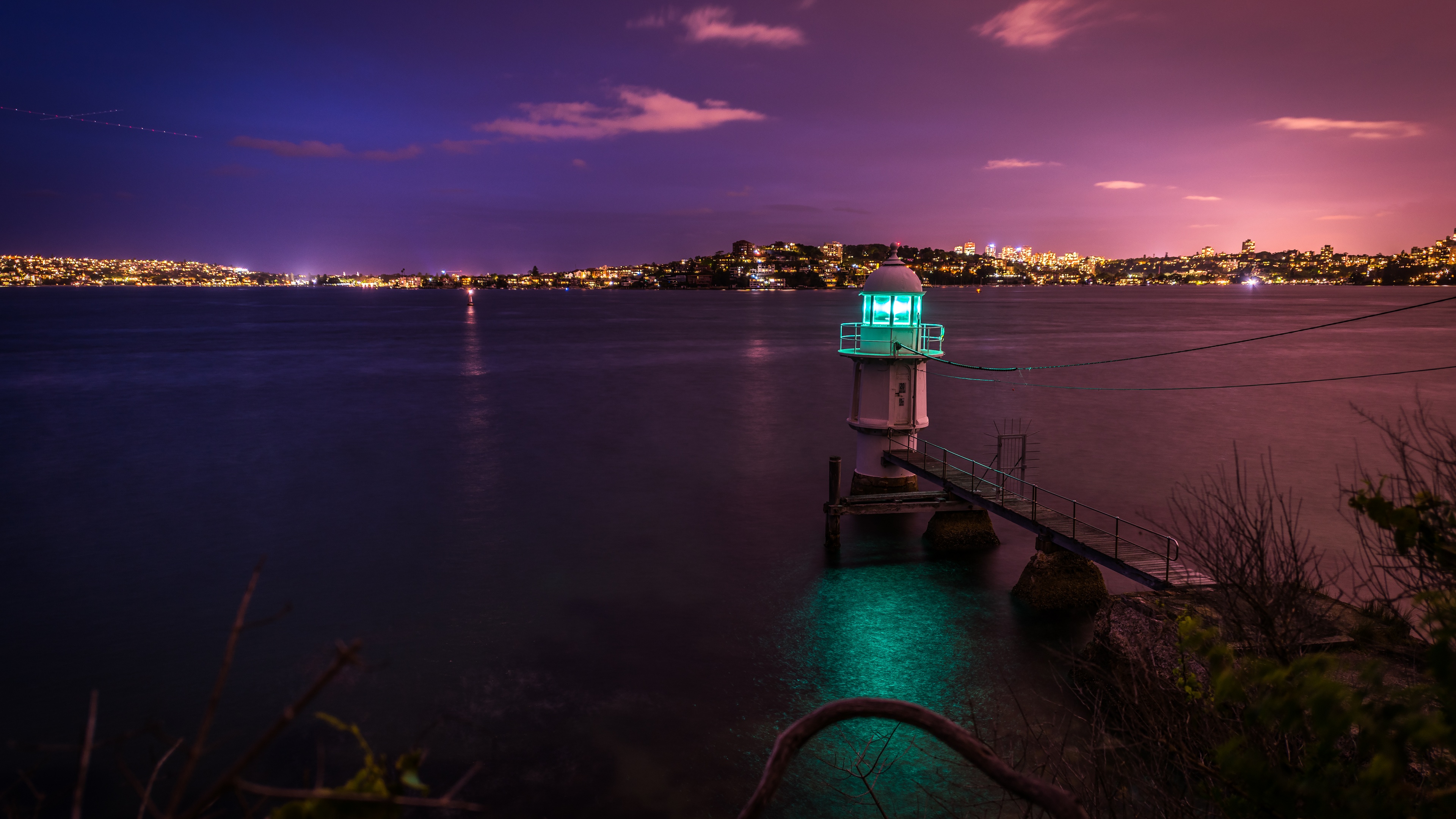A lighthouse overlooking the sparkling city lights of Sydney Harbour, Australia, during dusk.