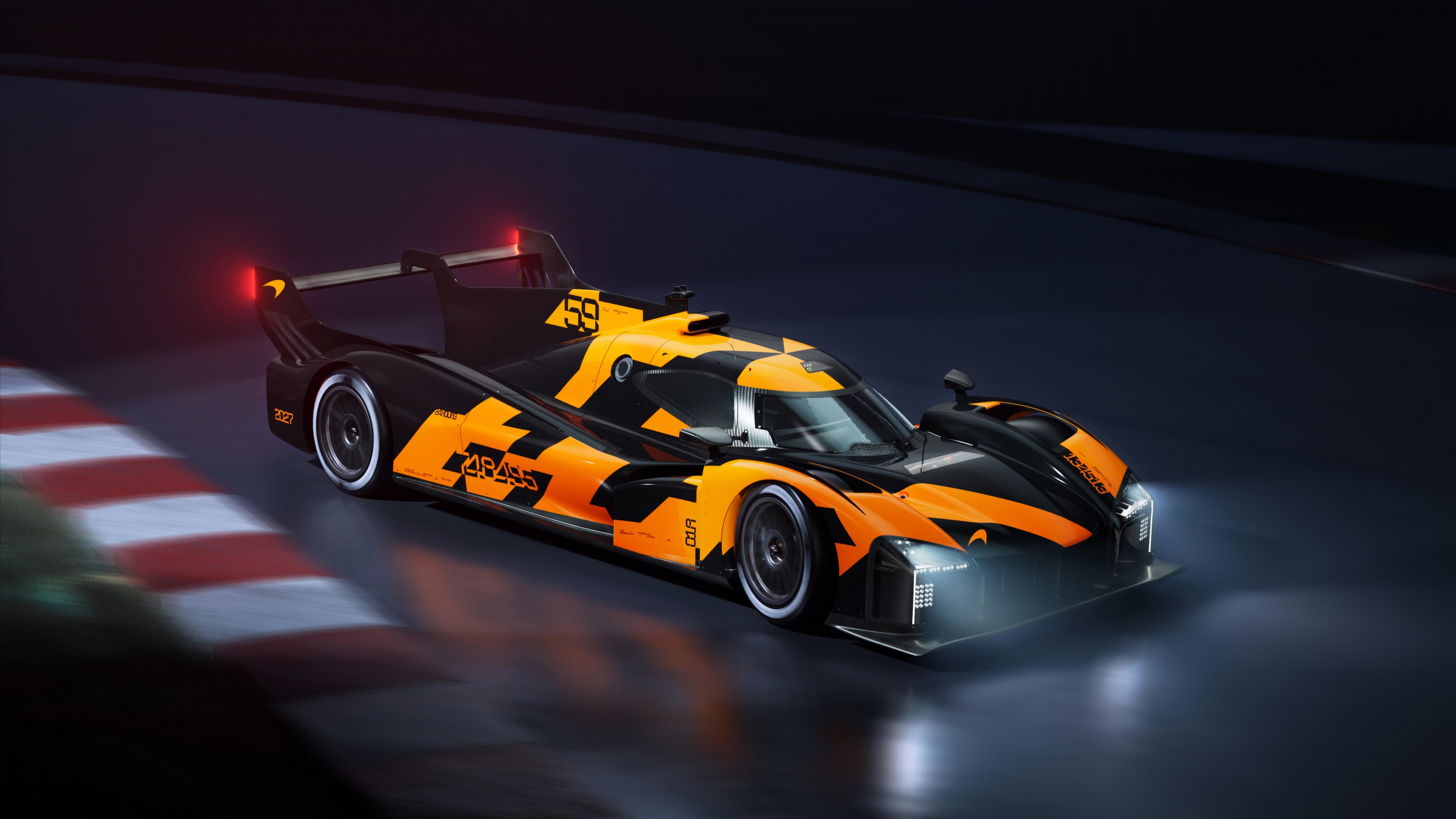 A group of bright orange race cars speeding around a dark race track at night under bright stadium lights.