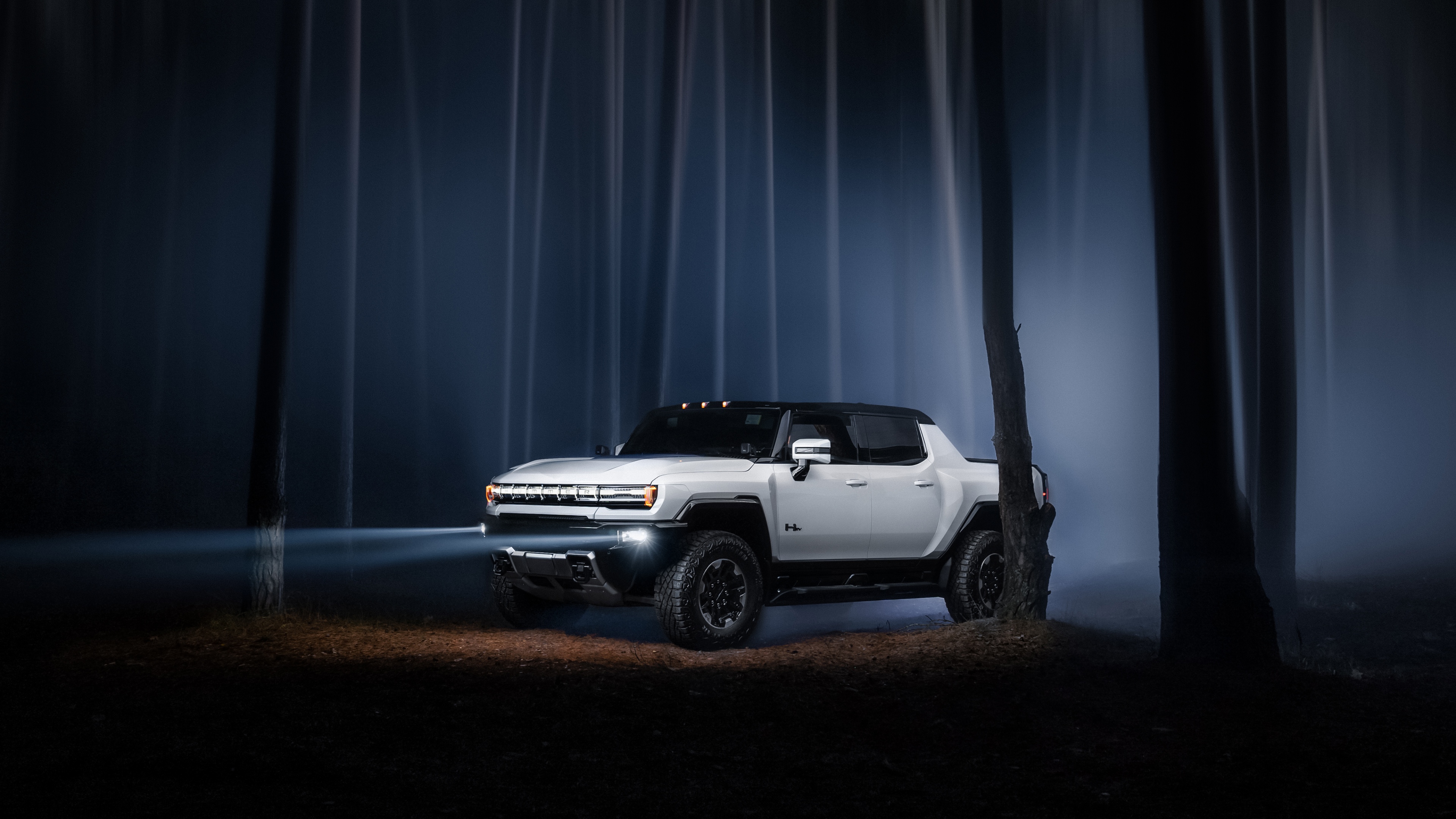 GMC Hummer EV electric vehicle with bright headlights navigating through a thick, foggy forest at night