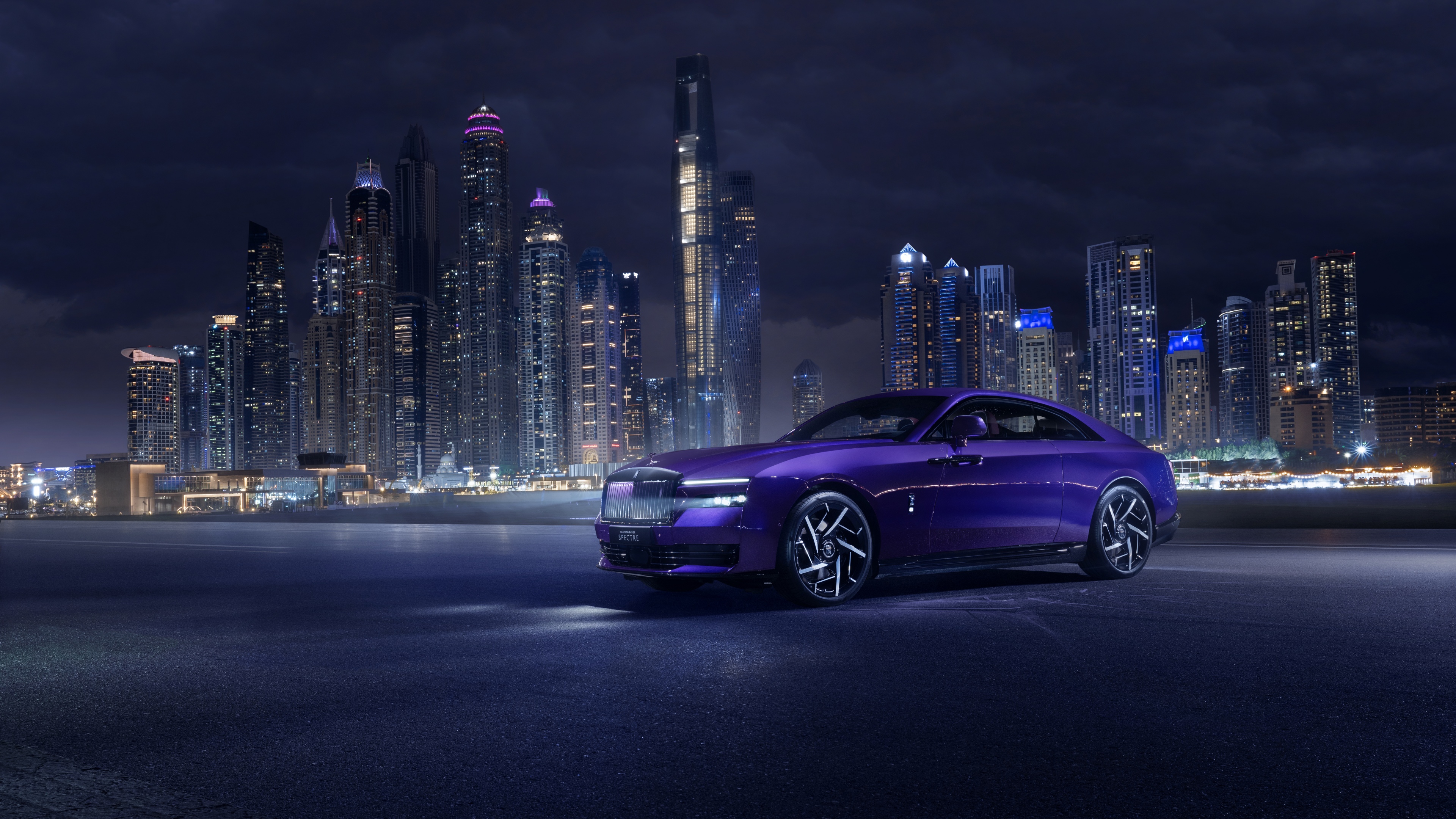 A luxury Rolls-Royce Black Badge Spectre parked in Dubai under a purple aesthetic night sky with city lights.