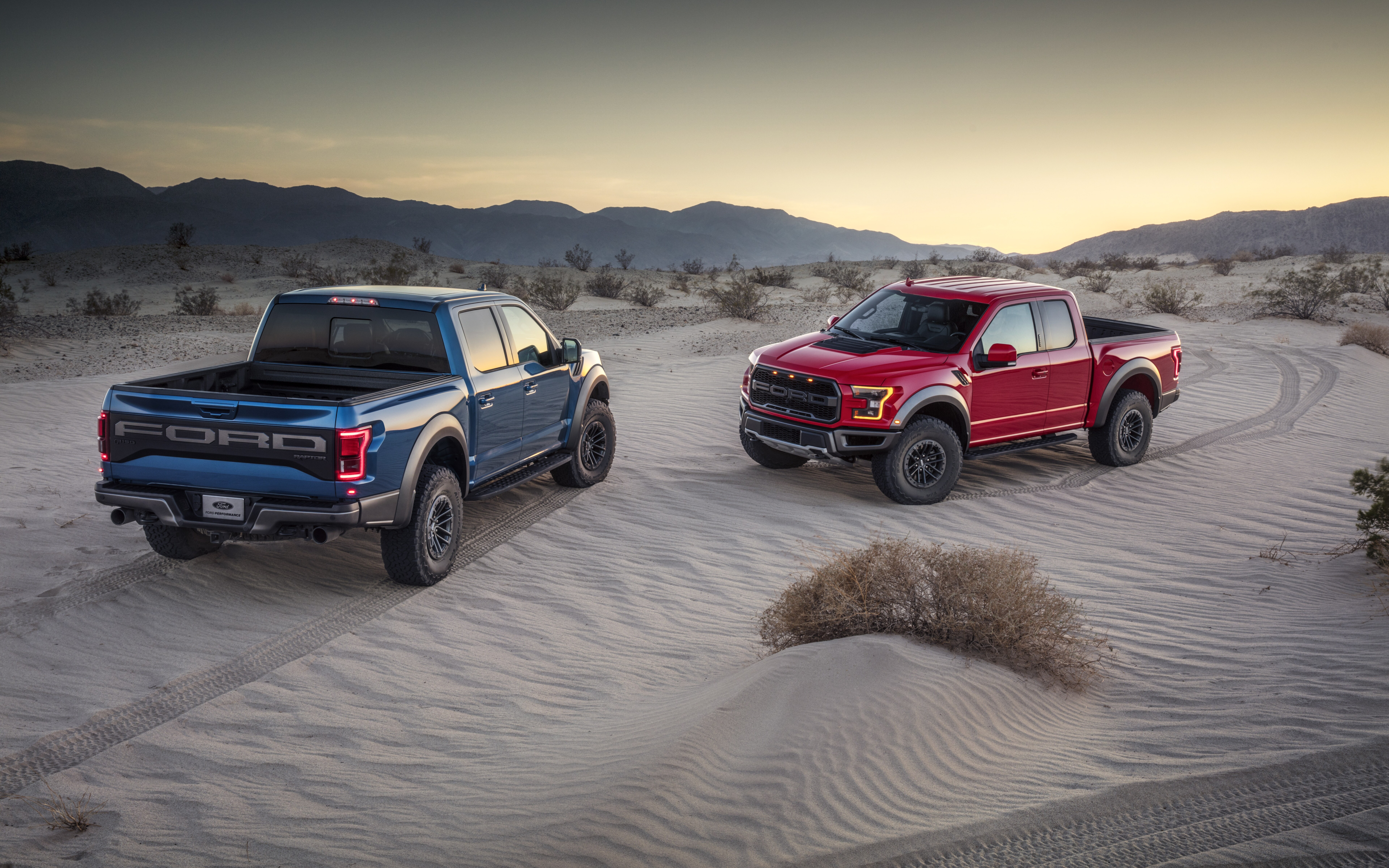 A Ford F-150 Raptor truck driving through a sandy desert landscape under bright sunlight.