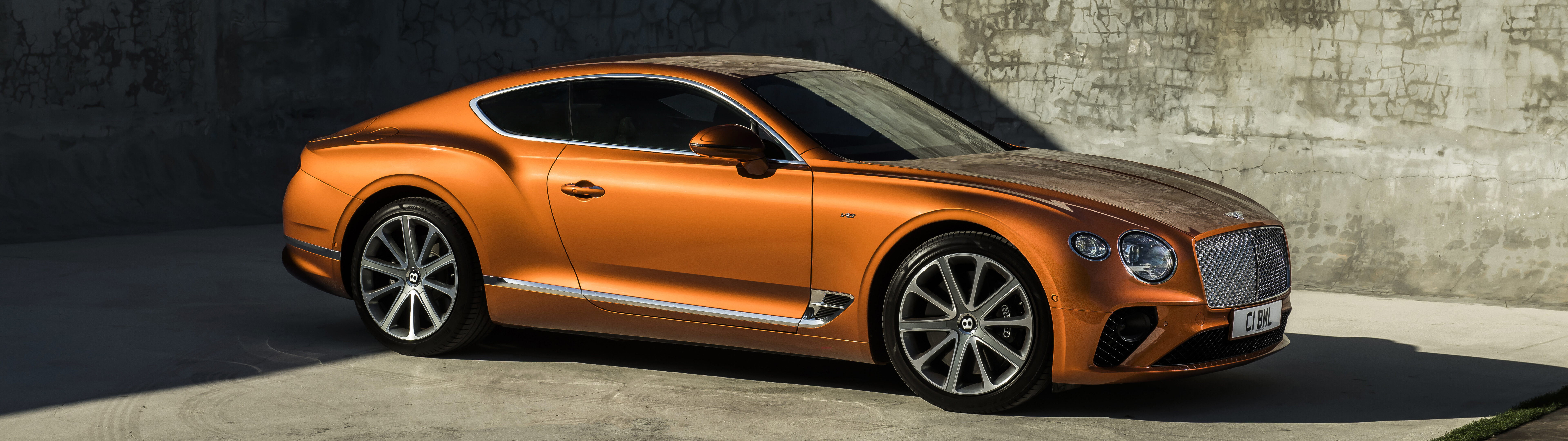 A glossy orange Bentley Continental GT luxury car parked in a scenic setting