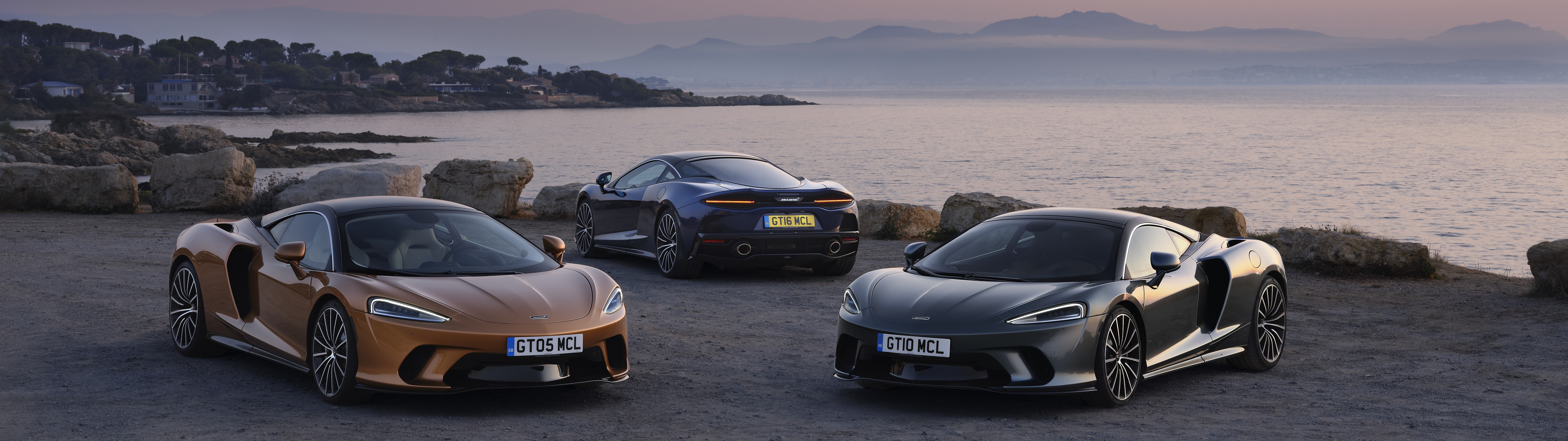Due supercar McLaren GT parcheggiate una accanto all’altra, una di colore argento metallizzato e l’altra di un vivace colore arancione.