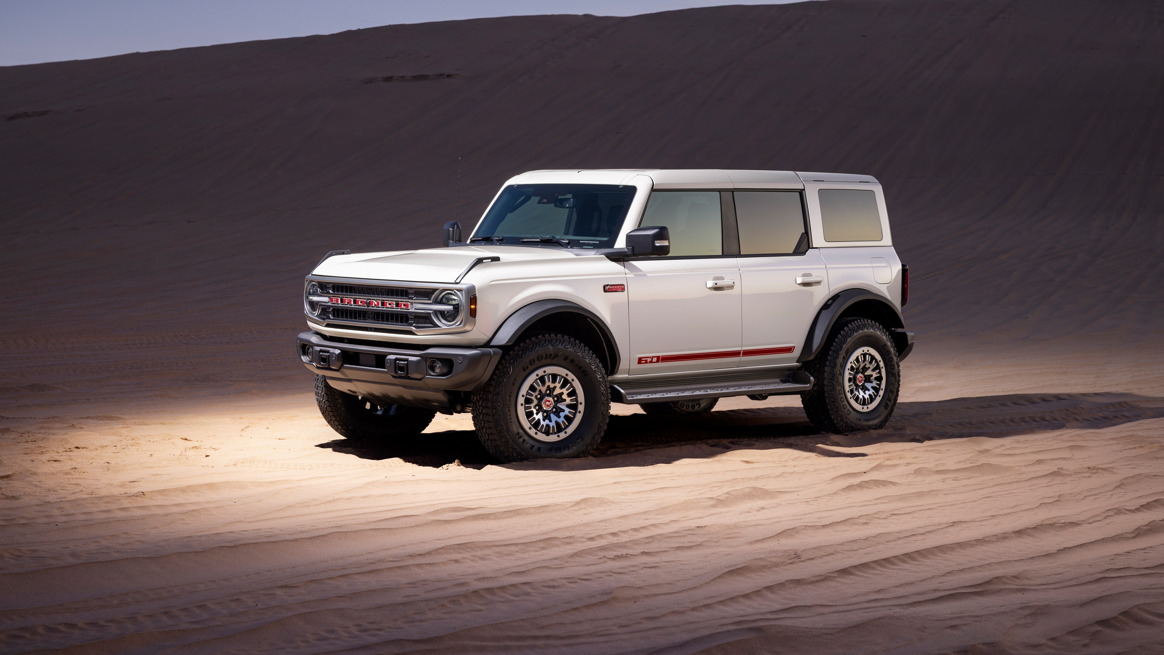 A futuristic 2026 Ford Bronco driving through vast, golden desert sand dunes.