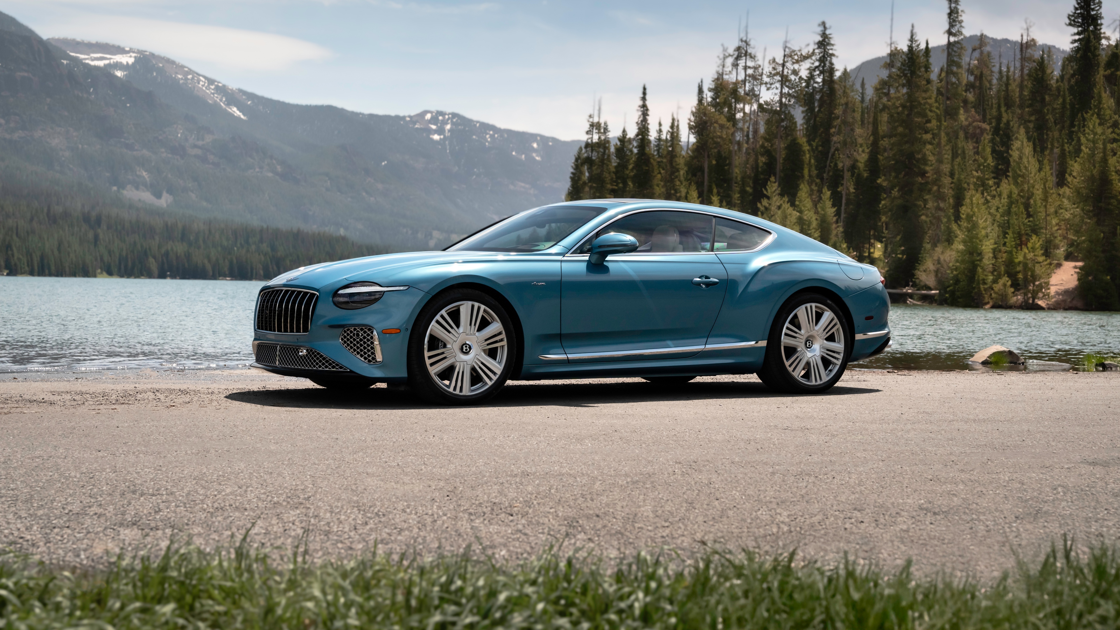 A blue Bentley Continental Car parked beside a serene mountain lake with alpine scenery.