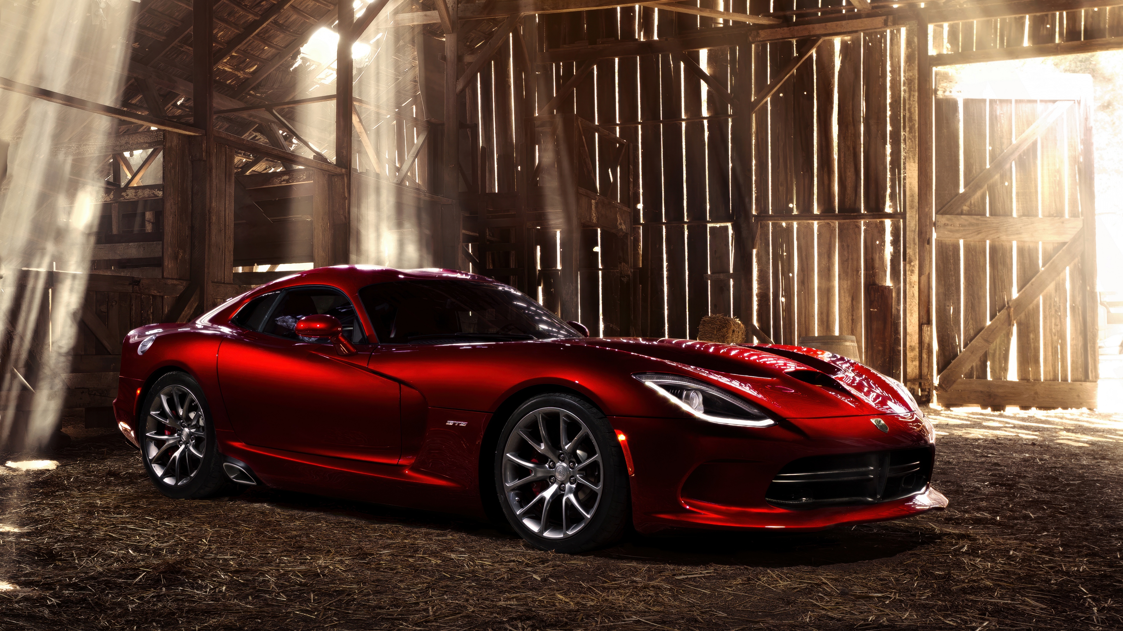 A vibrant red sports car parked inside a rustic wooden barn with golden sunlight streaming through the openings.