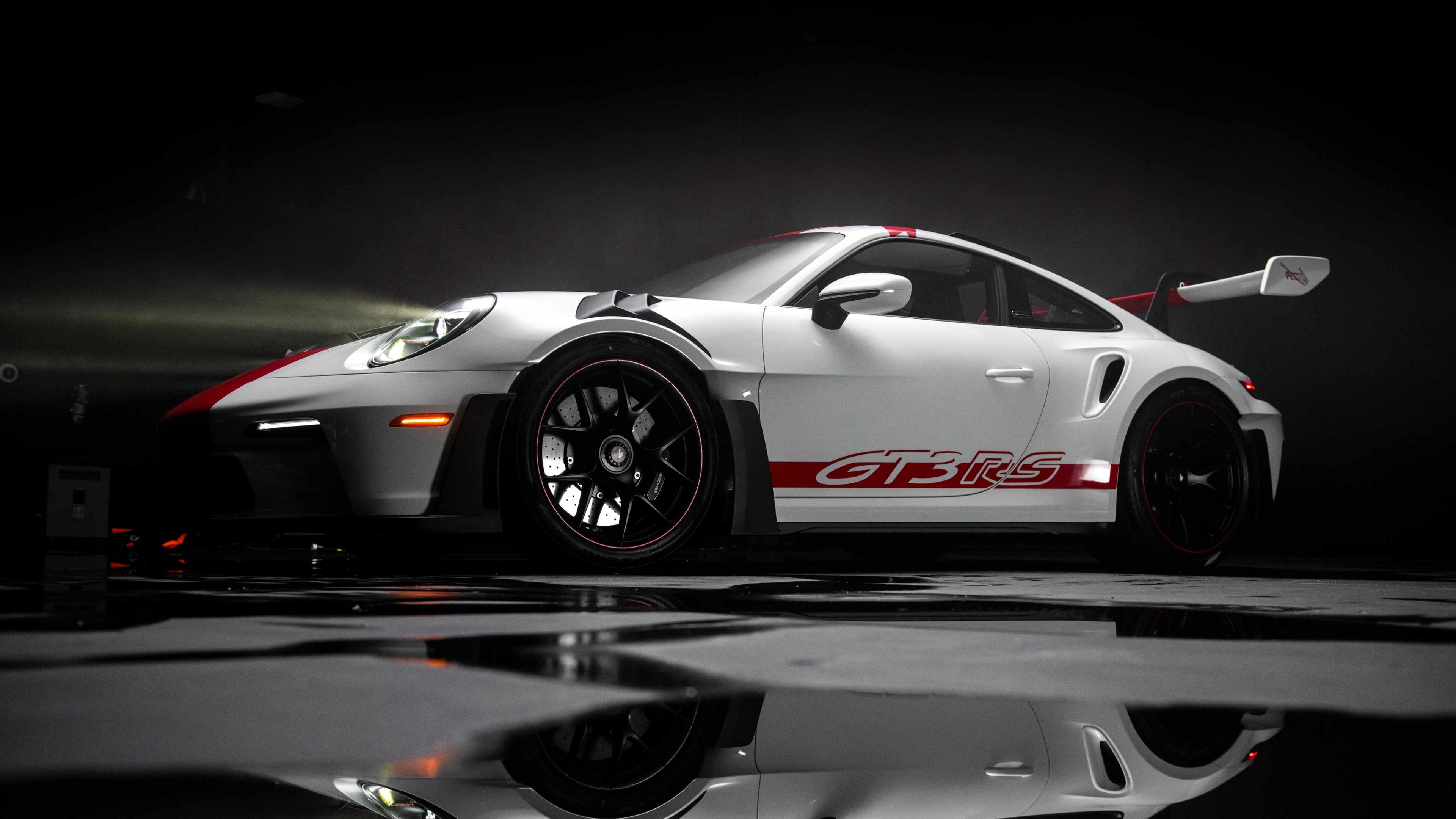 A sleek white Porsche 911 GT3 RS sports car positioned against a dark, moody background with light reflections on its body.
