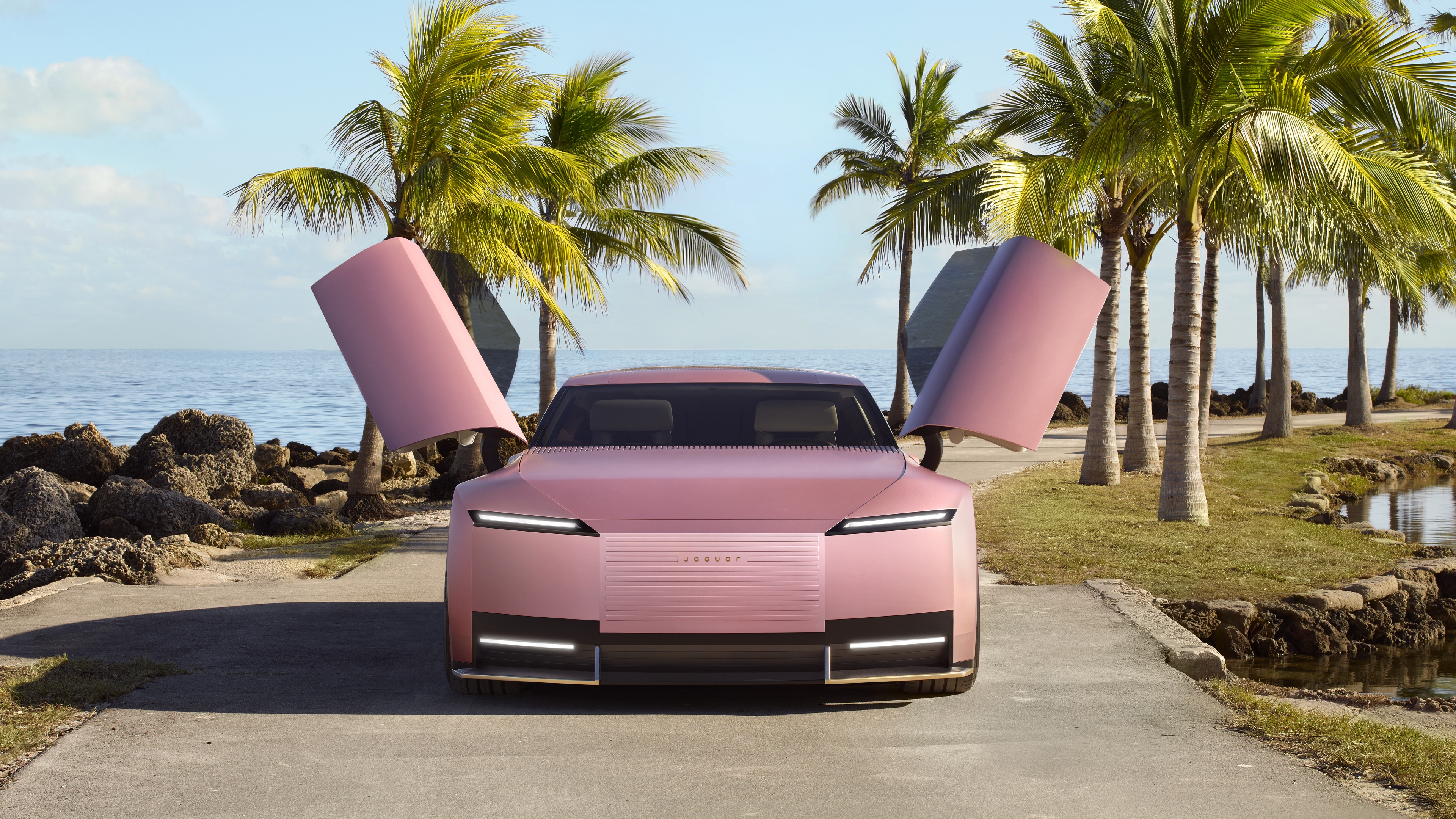 A sleek, futuristic Jaguar Type 00 electric concept car driving through a neon-lit Miami street with advanced skyscrapers and palm trees.