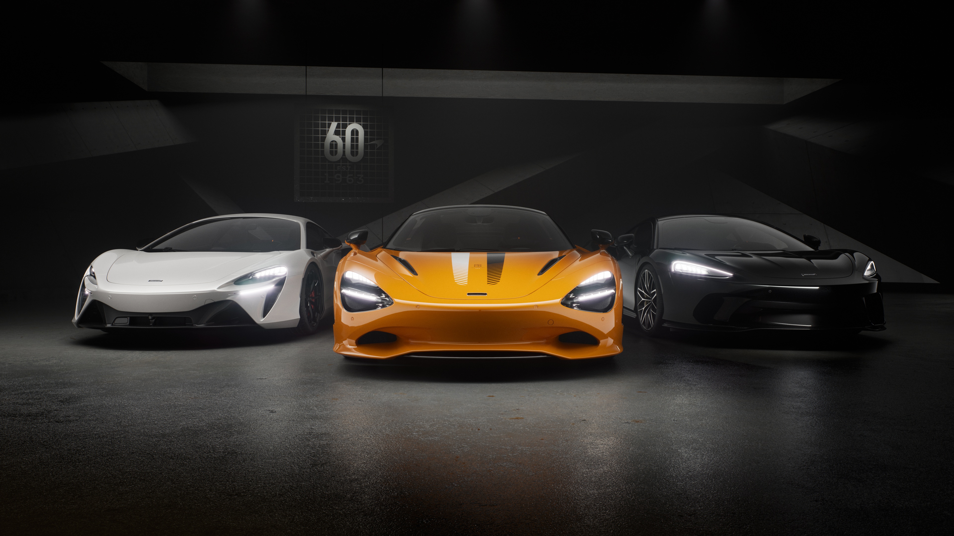 A group of three McLaren supercars, including the Artura, 750S, and GT, displayed against a dark, minimalist background.